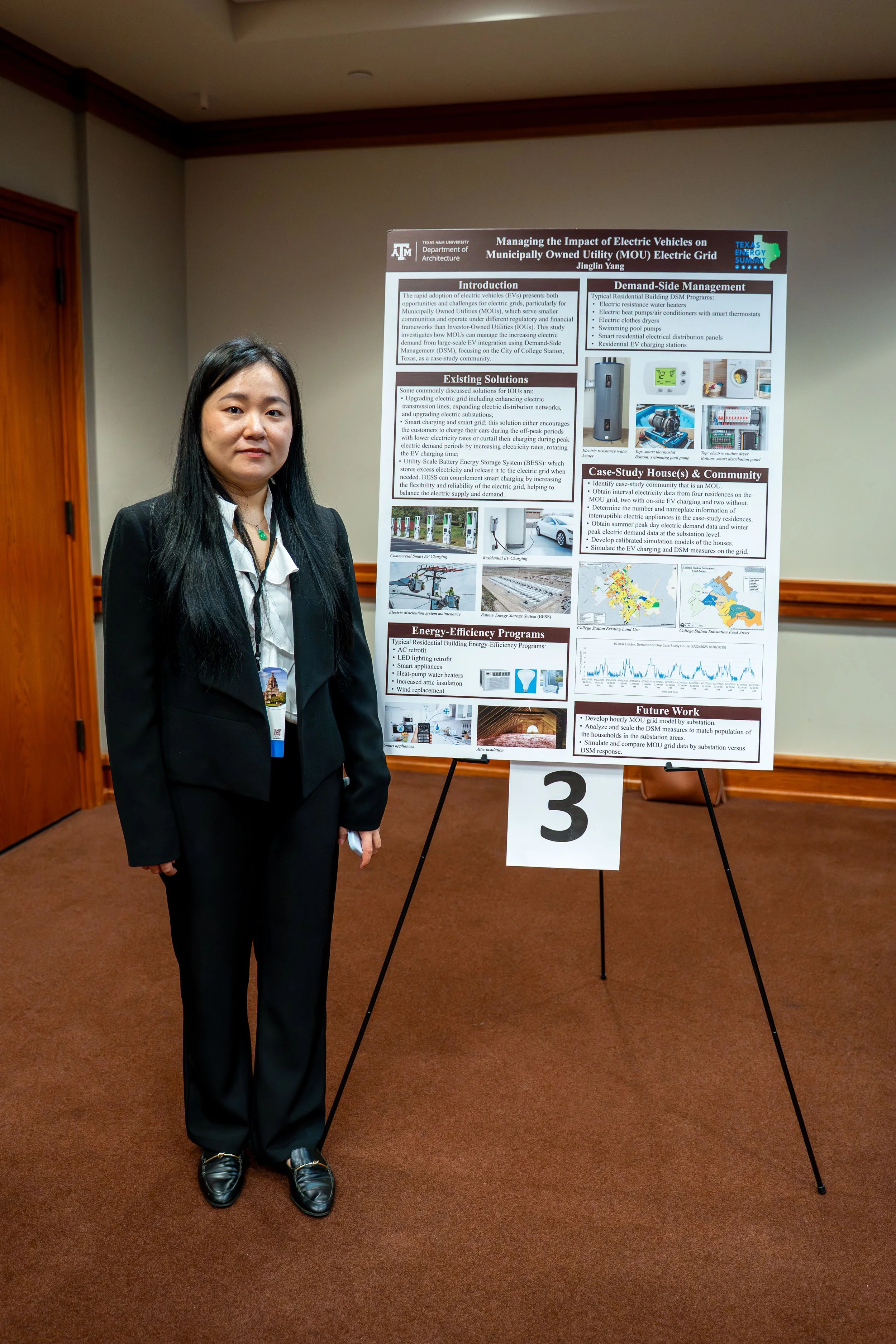 A woman in a black suit standing next to a research presentation poster on a stand at a conference.