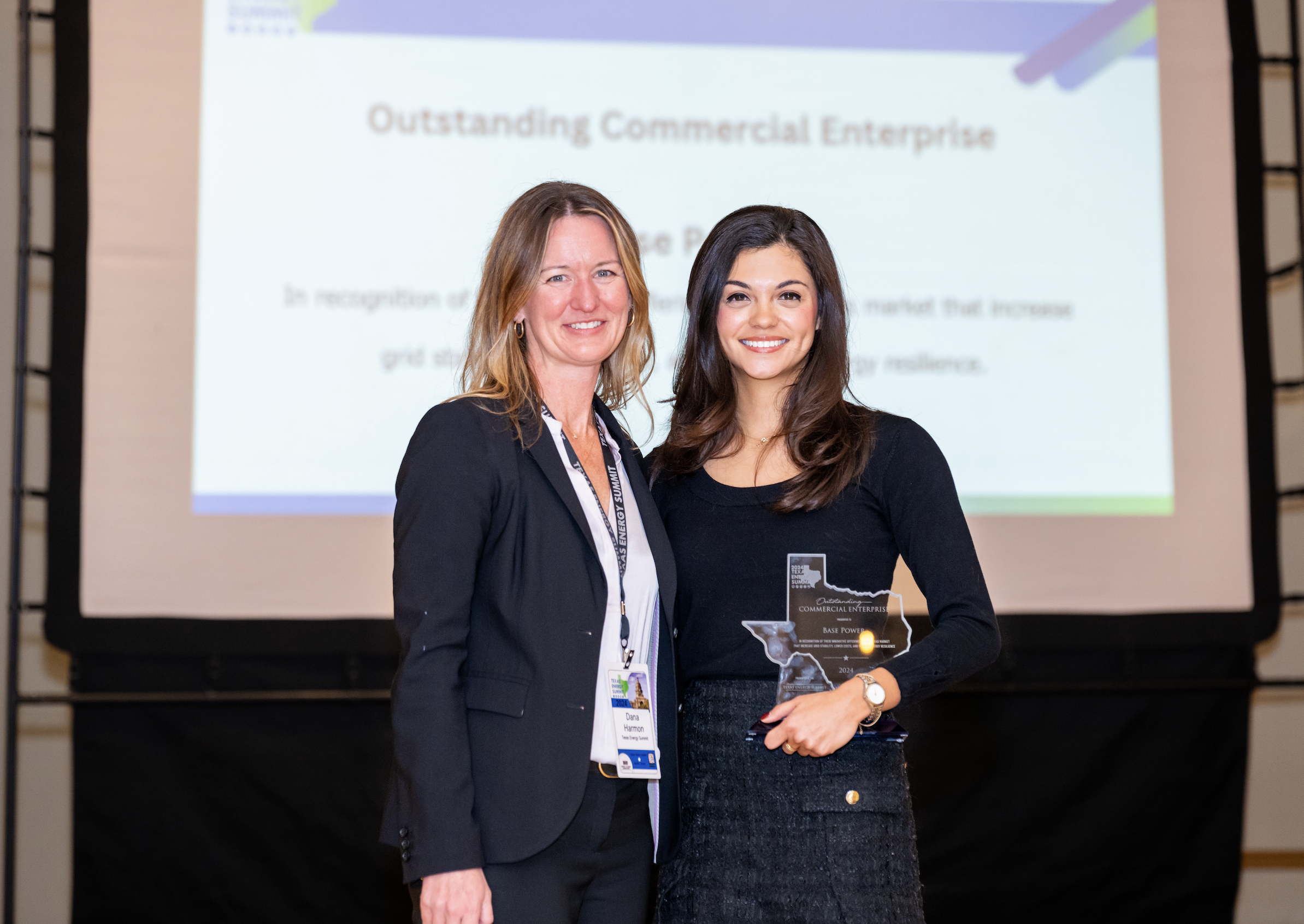 Two women standing together at an award ceremony, with a woman holding a glass award shaped like Texas and a presentation screen in the background displaying "Outstanding Commercial Enterprise."