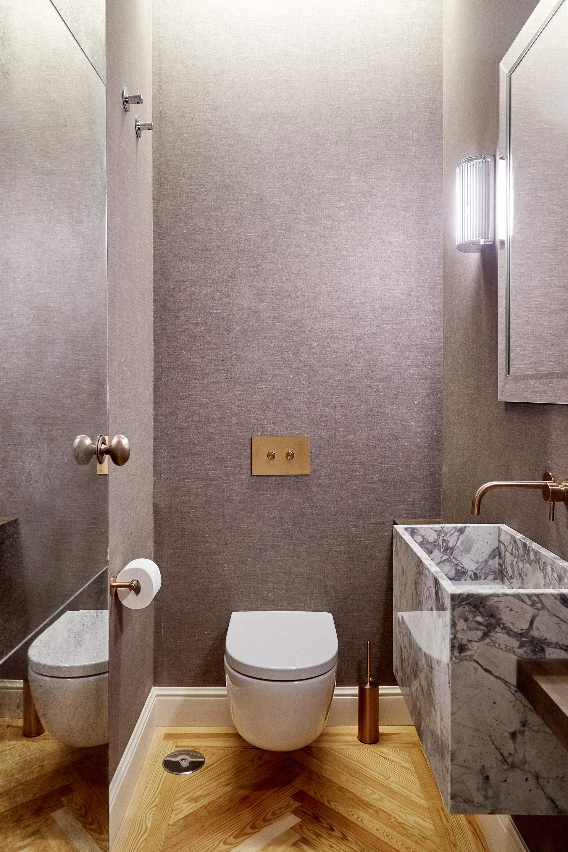 Inodoro en un baño moderno con paredes gris oscuras, lavabo de mármol y accesorios dorados.