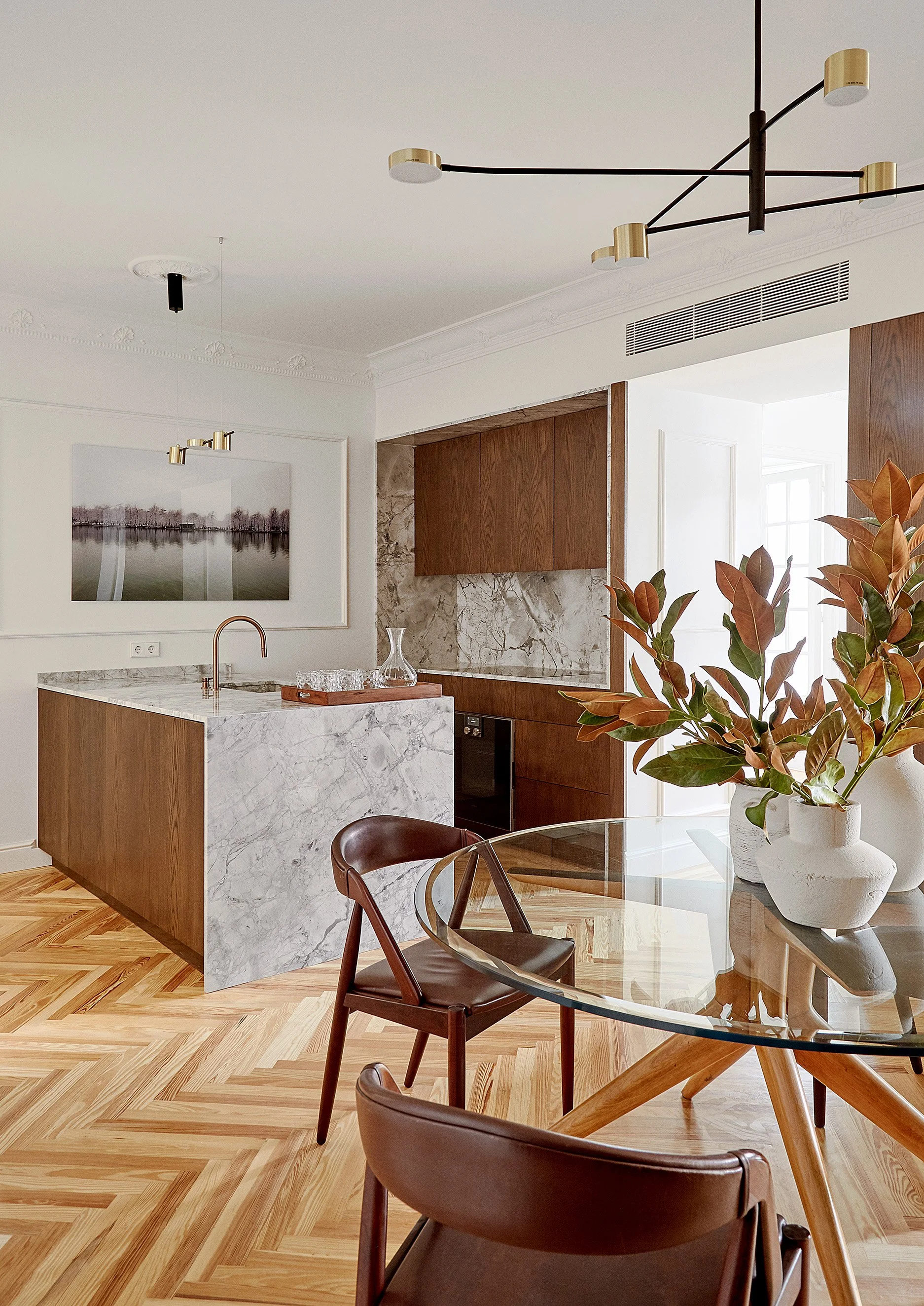 Interiores de cocina y comedor con muebles de madera, encimera de mármol, plantas en macetas, mesa de cristal y sillas de cuero.