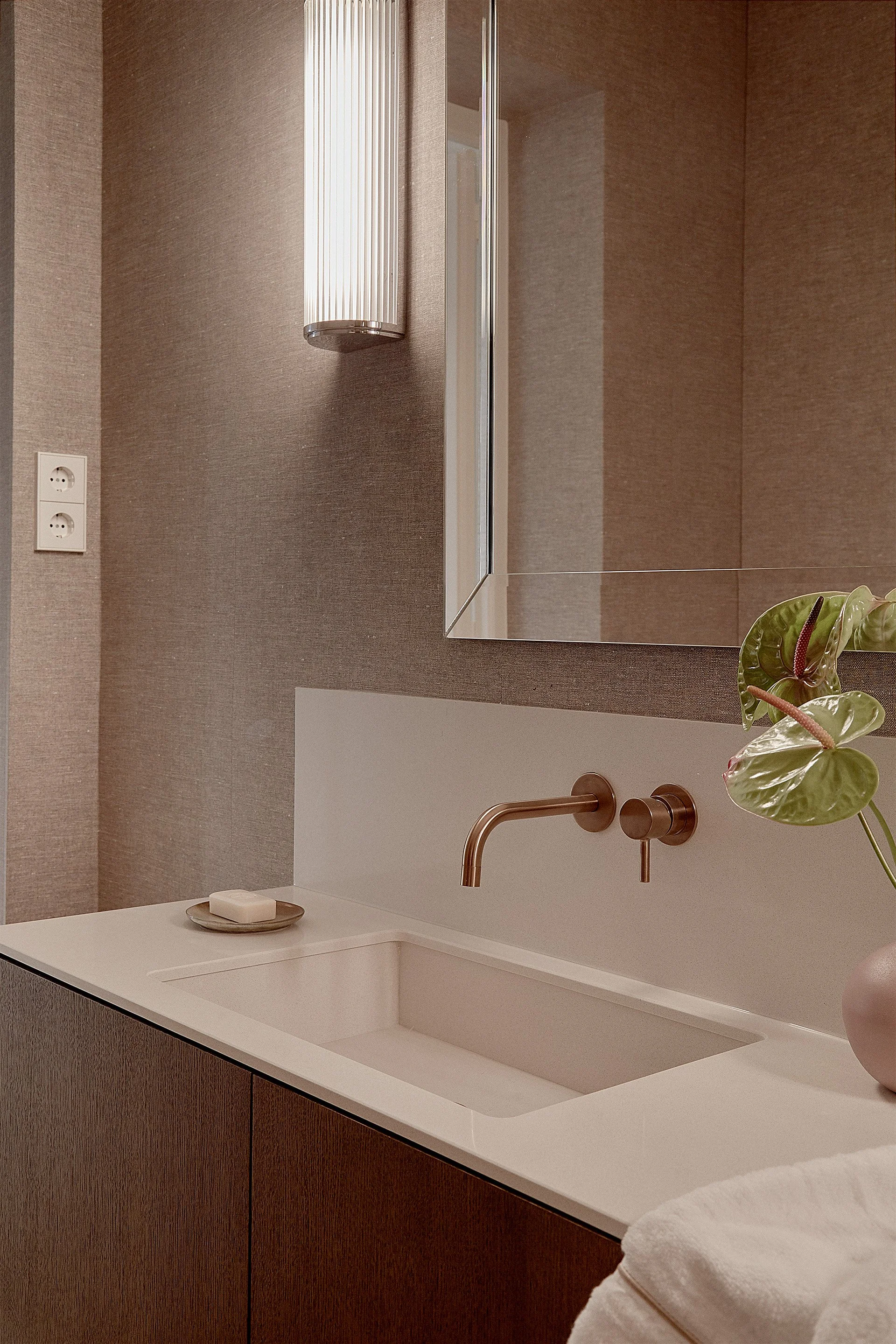 Lavabo blanco en lavabo de madera con espejo y planta decorativa junto a la llave de agua en un baño moderno.