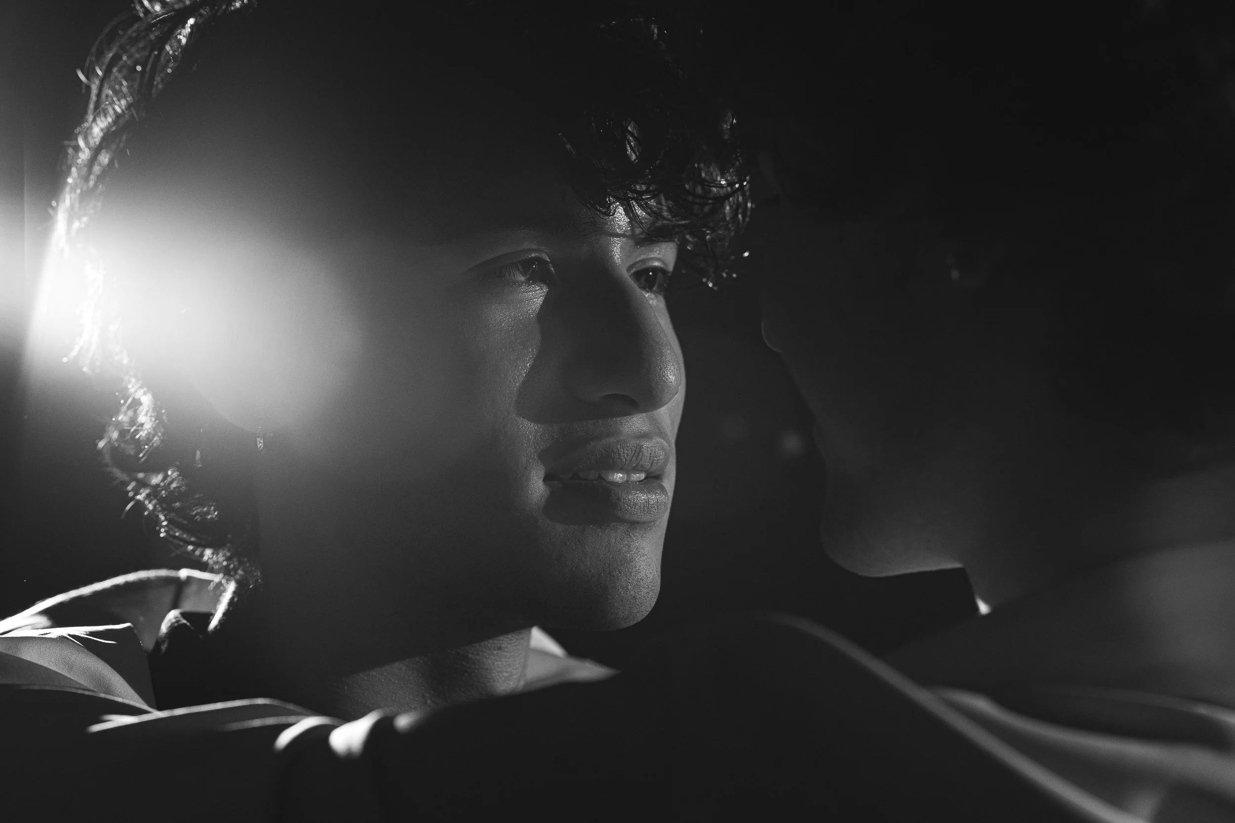 theatrical lighting of male couple, focused on one person in black and white.