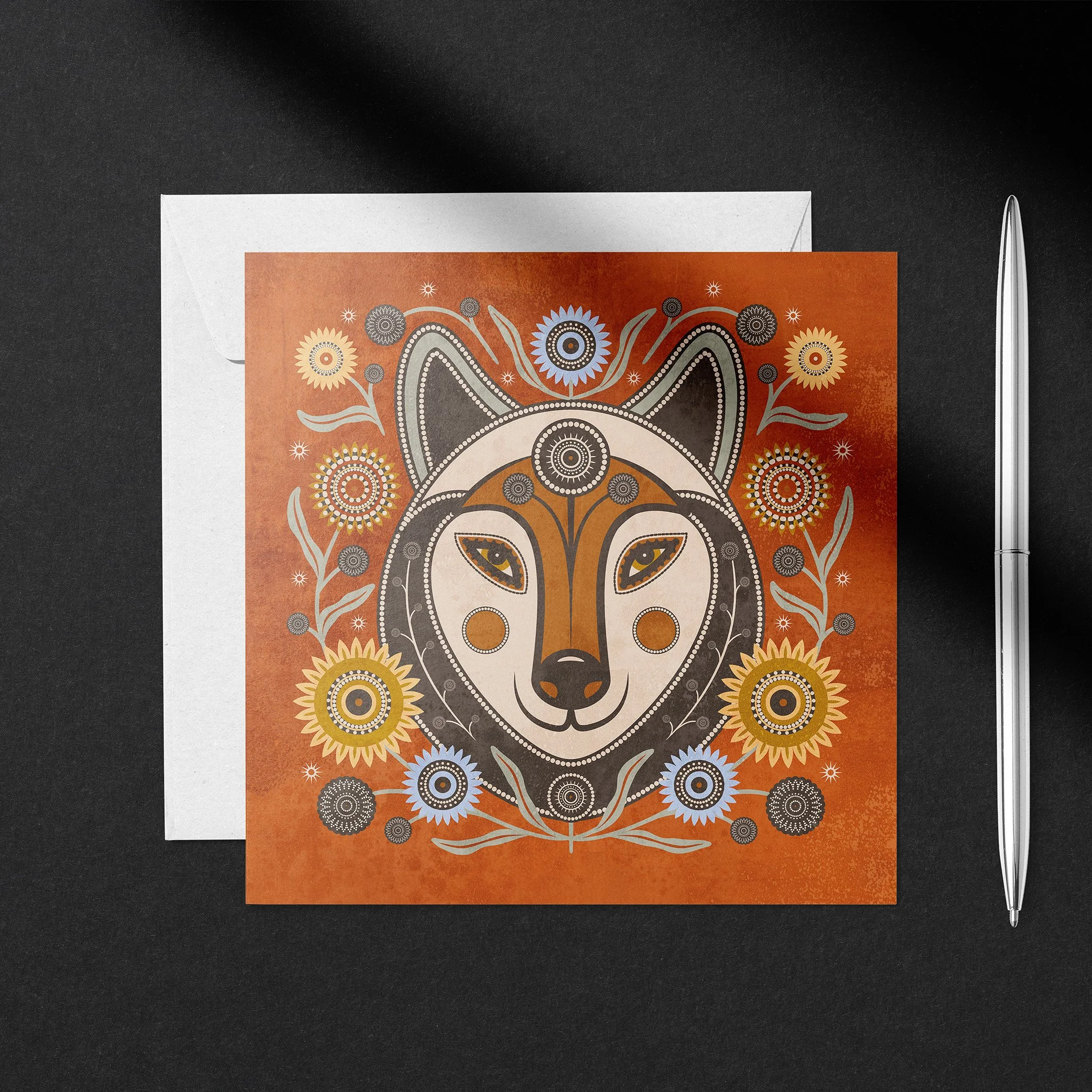 Floral folk-inspired wolf greeting card shown with blank envelope and pen on dark background.