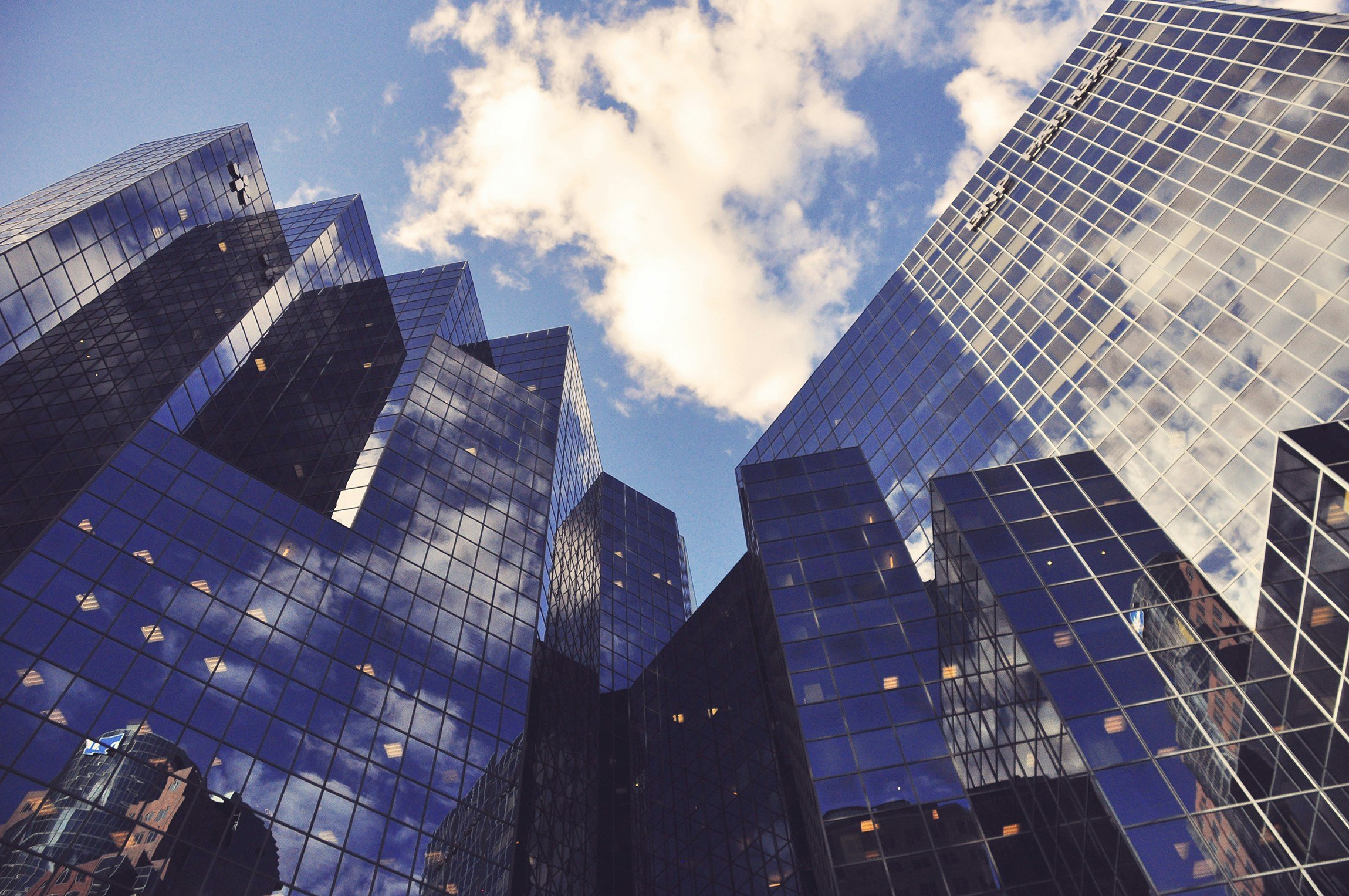 Low-angle view of modern glass skyscrapers reflecting clouds and sky in a city.