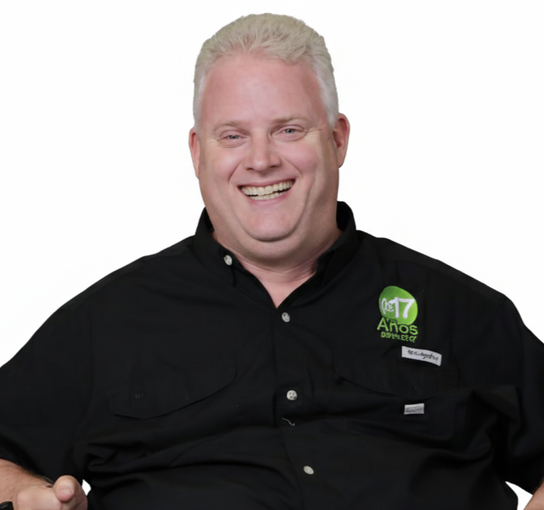 Man with short, light-colored hair smiling, wearing a black collared shirt with a green and white logo celebrating 17 years on the chest.