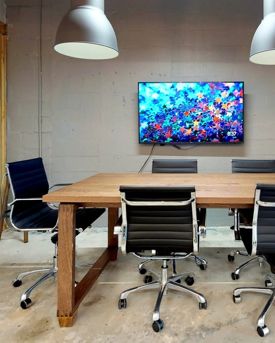 Huddle Room meeting space at Brainbox Coworking in Midtown Miami with wooden conference table, wall-mounted screen, and modern lighting for professional team meetings.