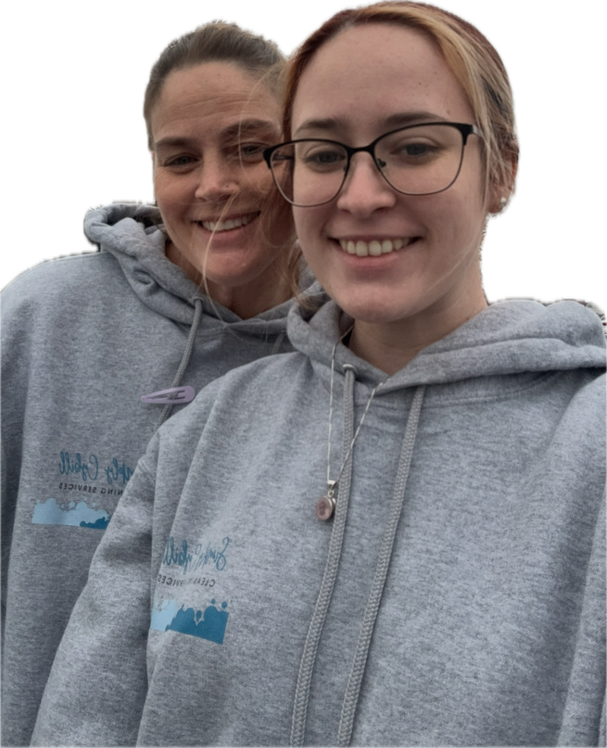 Two young women smiling, wearing matching gray hoodies with logo, outdoors.