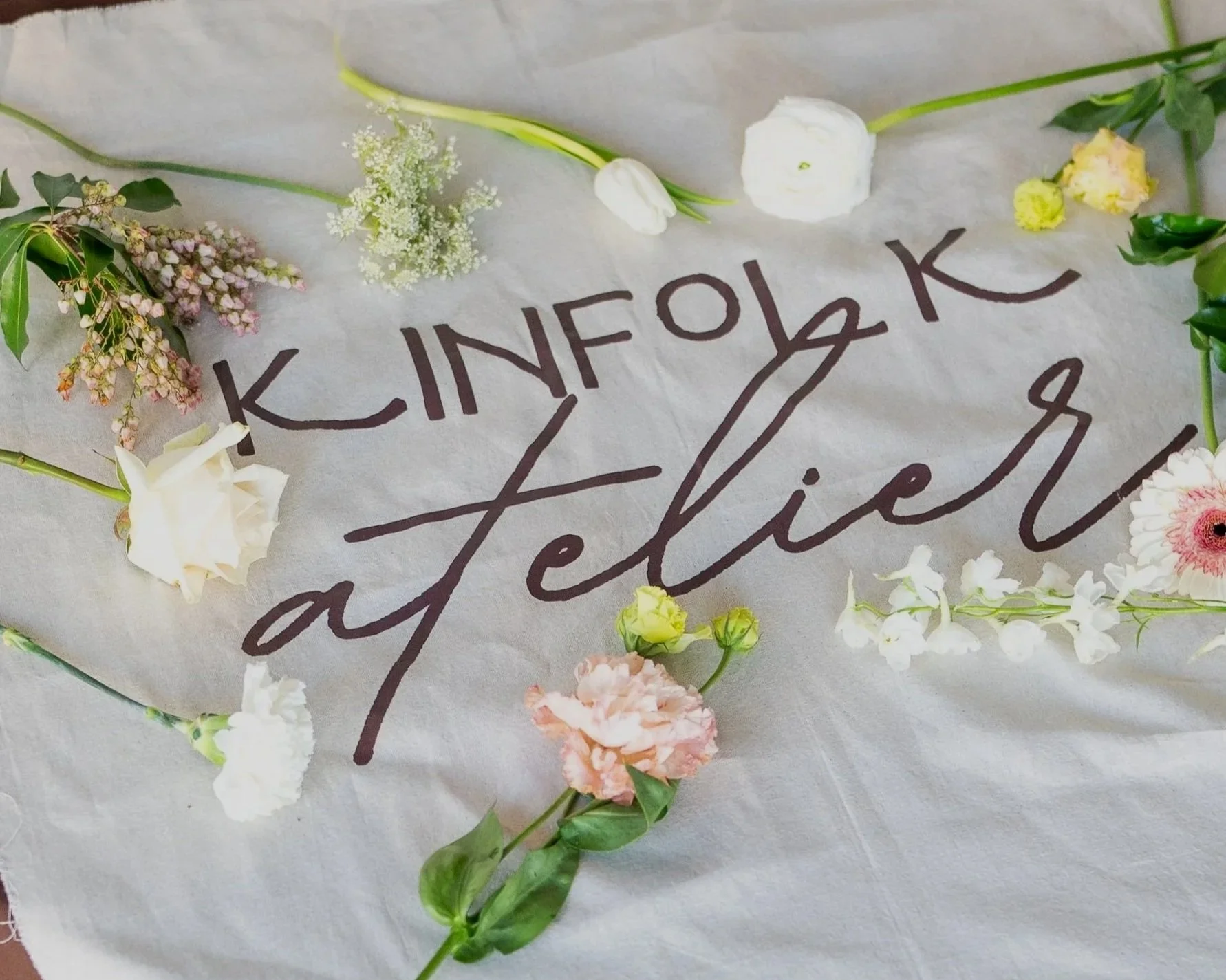 Flowers aesthetically arranged around the words 'Kinfolk Atelier'.
