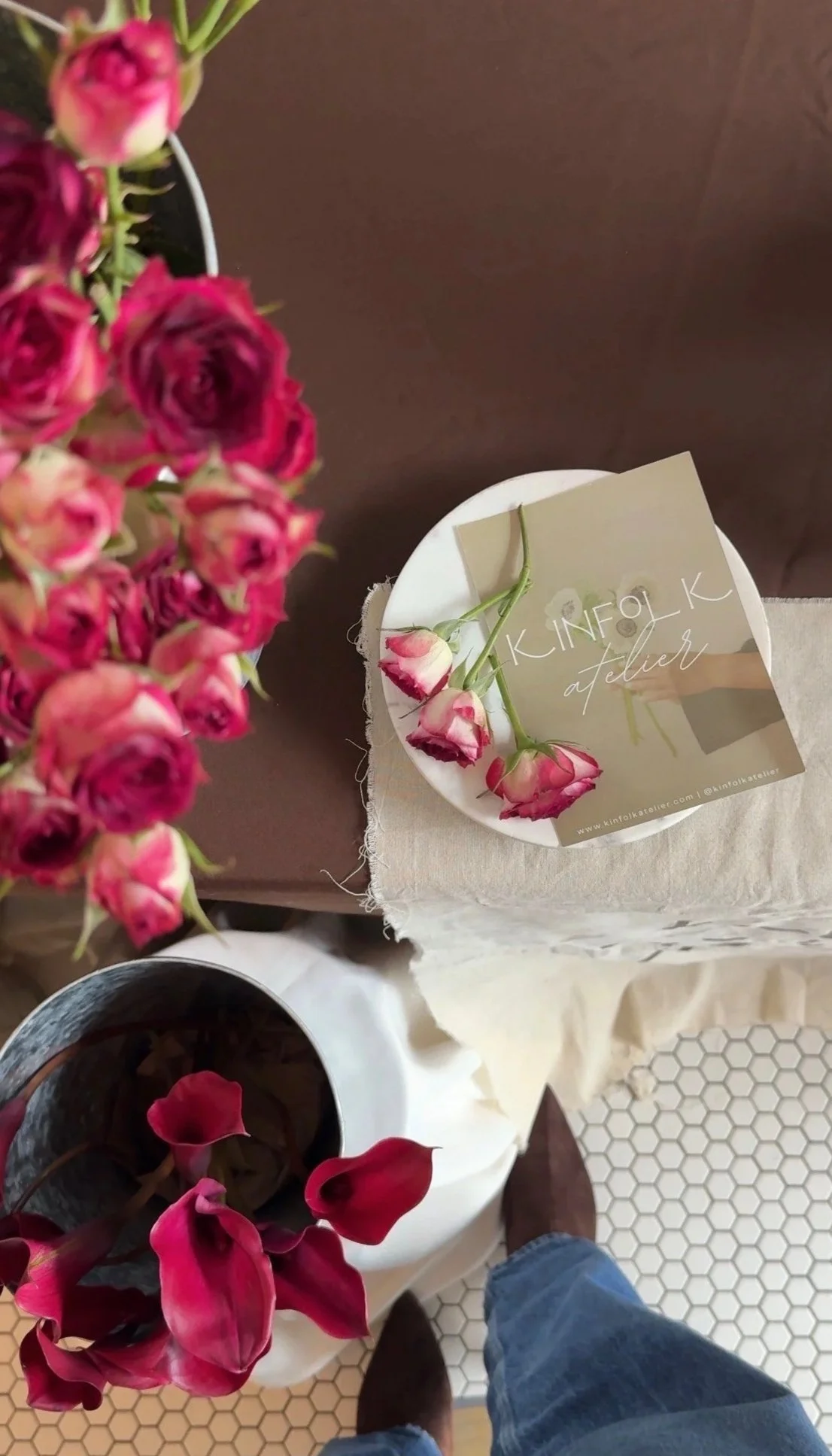 Arrangement of pink and red roses and calla lilies in a vase on a table with a card that says 'KINFOLK atelier'.