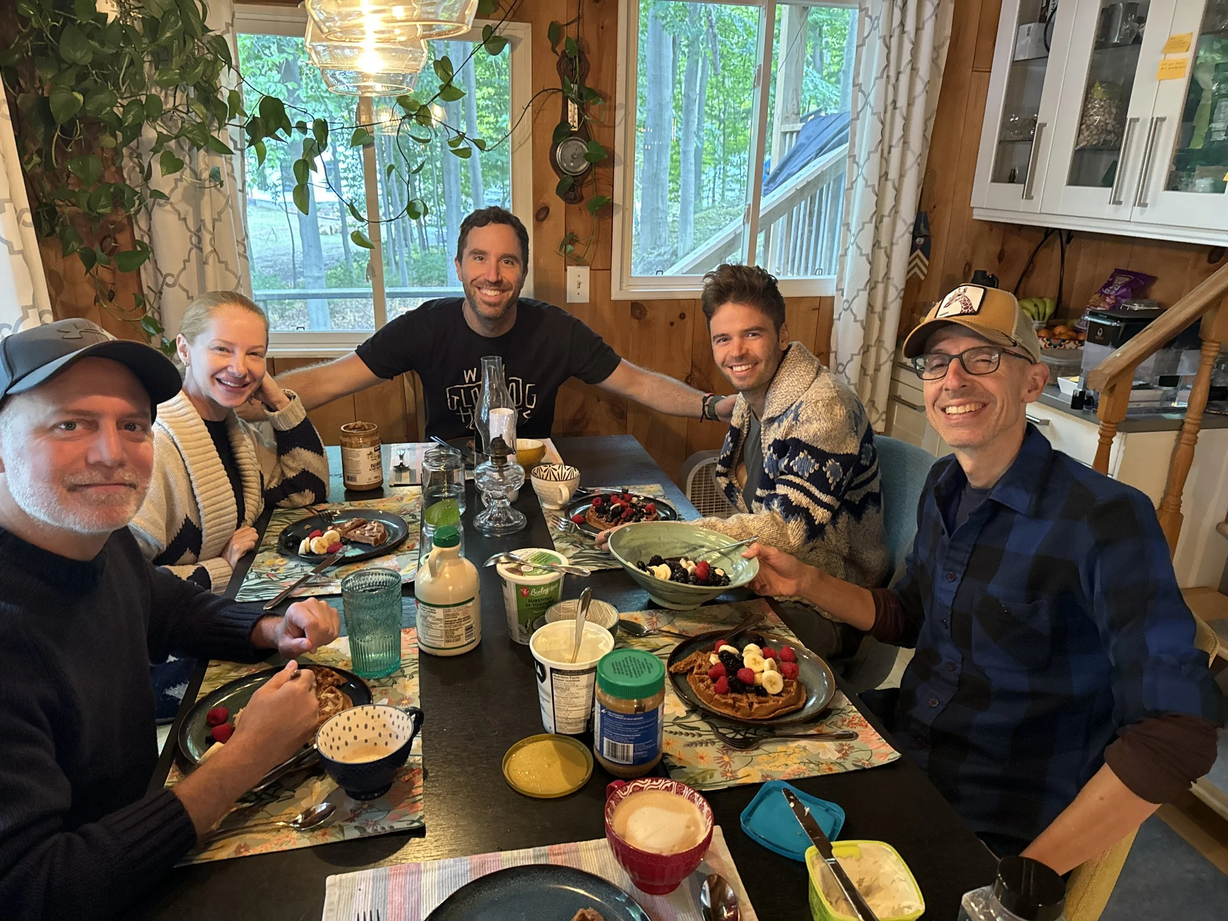 Group of people smiling and eating breakfast together at a table.