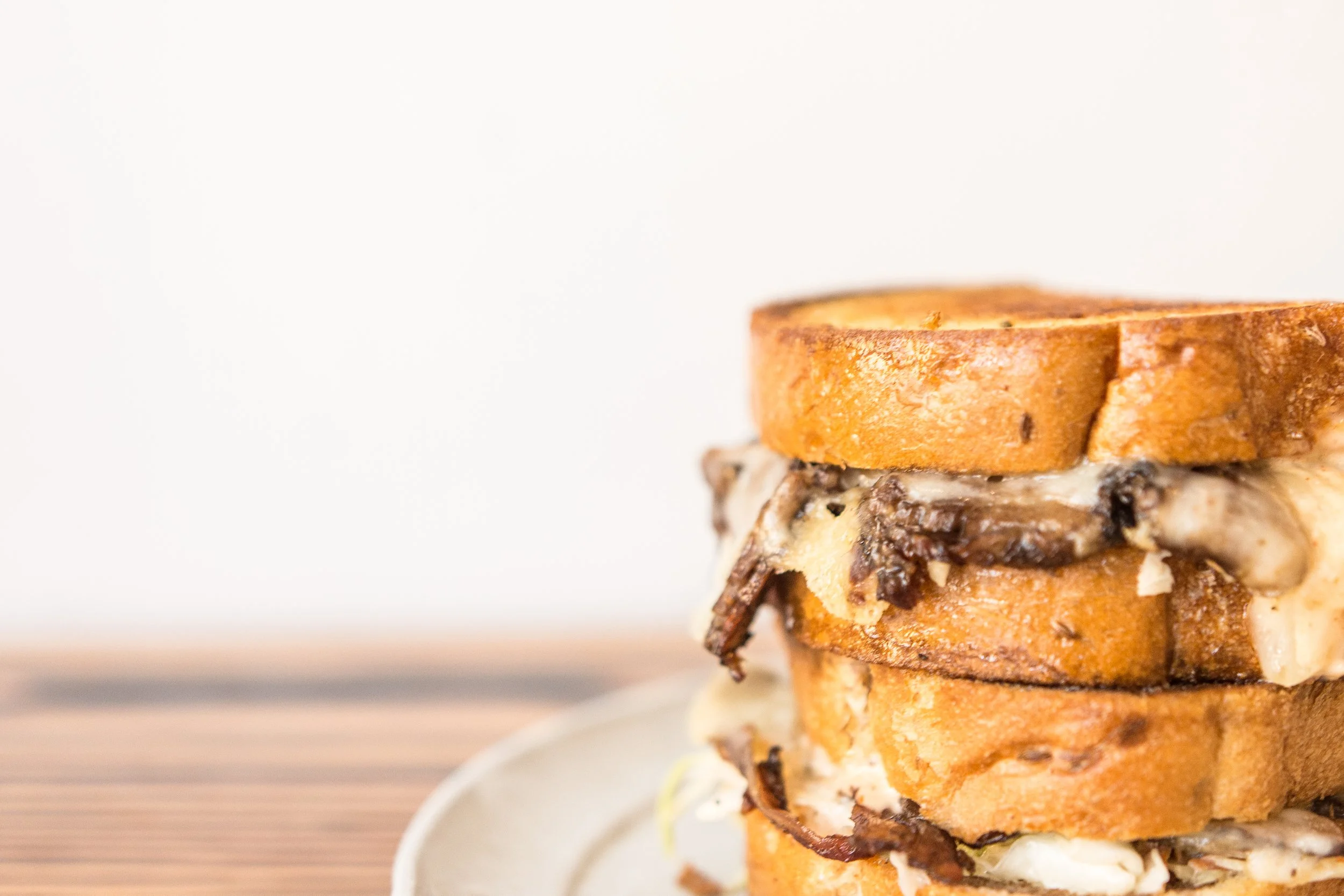 Close-up of a stack of grilled cheese sandwiches with mushroom filling on a plate, on a wooden surface with a white background.