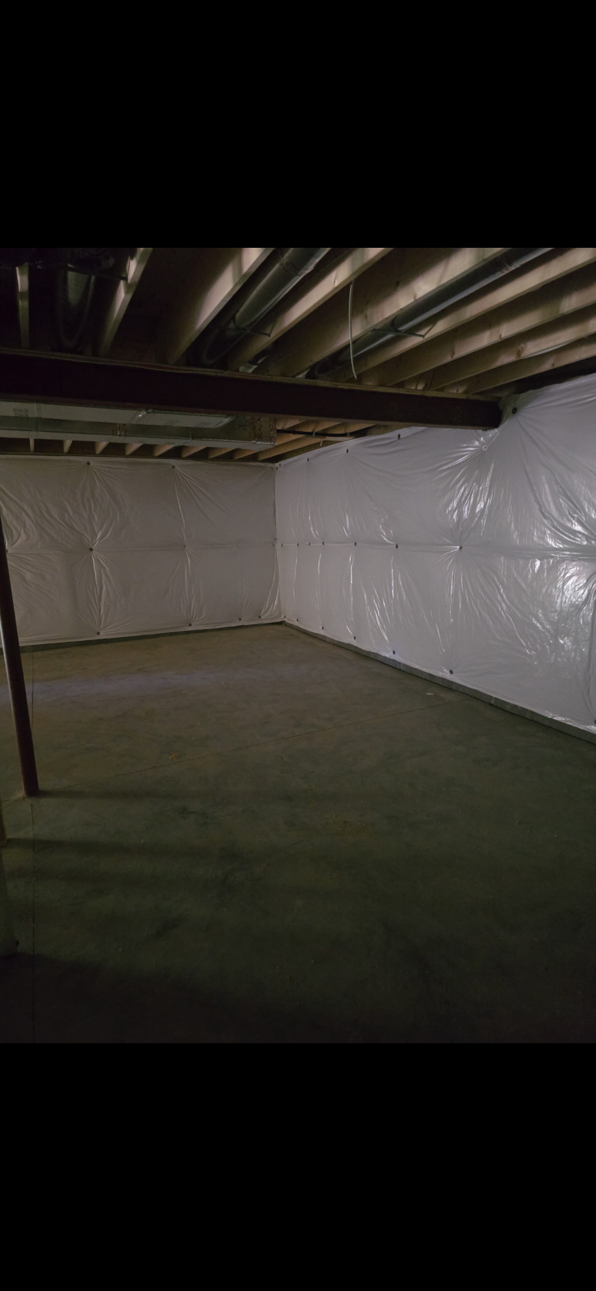 Empty basement with unfinished wood ceiling, exposed ducts, concrete floor, and plastic sheeting covering the walls.