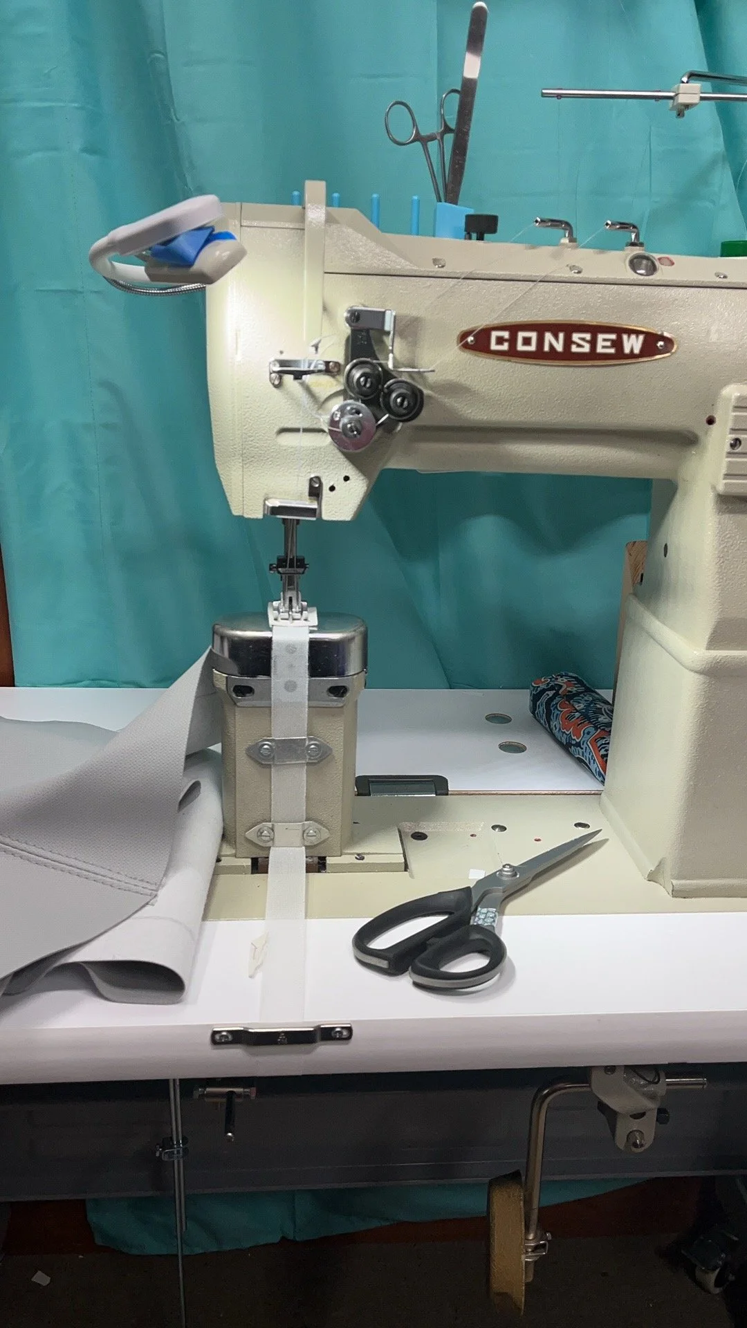 Industrial twin needle post bed sewing machine with scissors, fabric, and sewing tools on a work table.