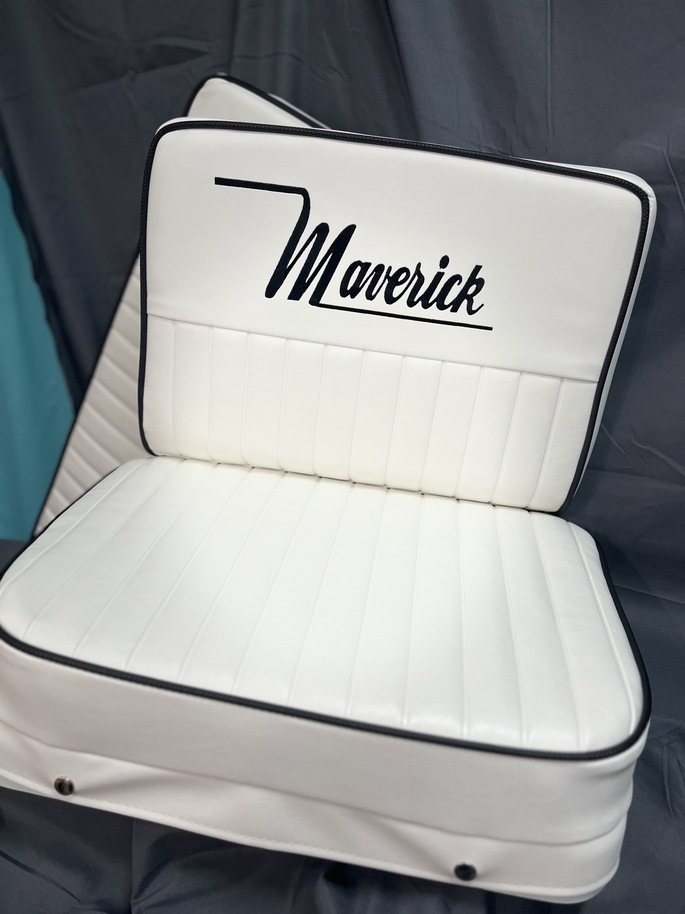 A white padded seat with the word 'Maverick' embroidered in black on the backrest.