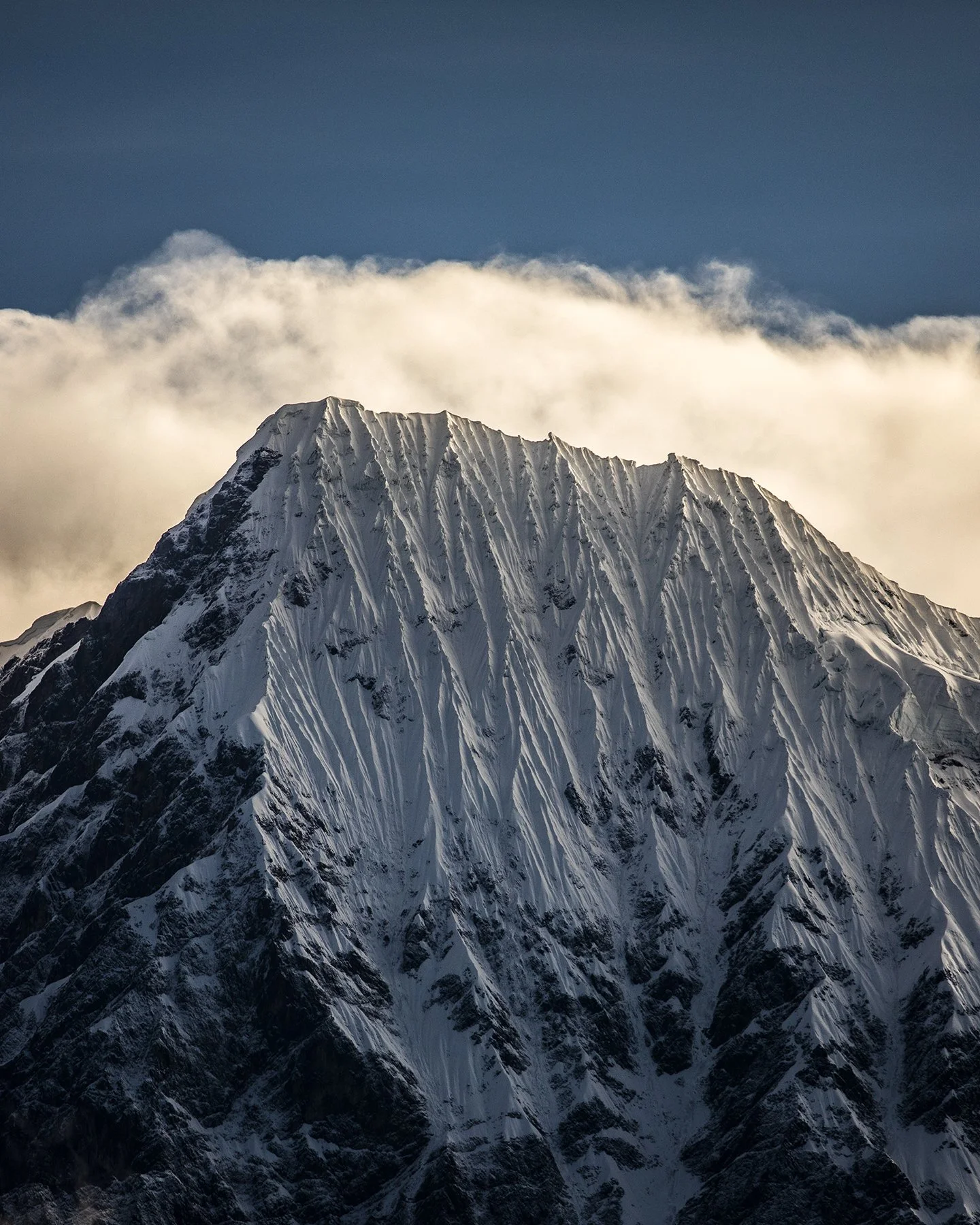 Montaña cubierta de nieve con picos afilados y nubes en el cielo.