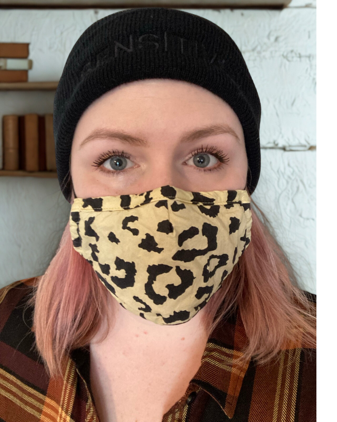 image of young white woman wearing a black beanie and animal print face mask. She is staring straight into the camera and has pink hair.