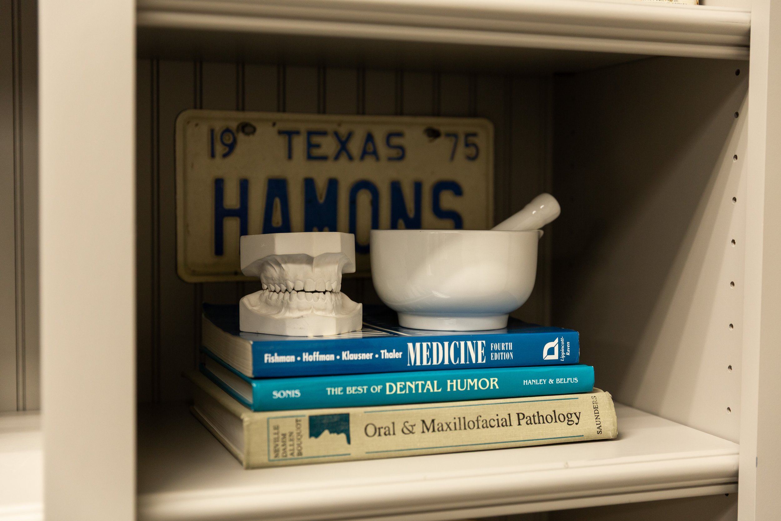A shelf with medical books, a dental model, and a dental mortar and pestle, with a Texas license plate in the background.