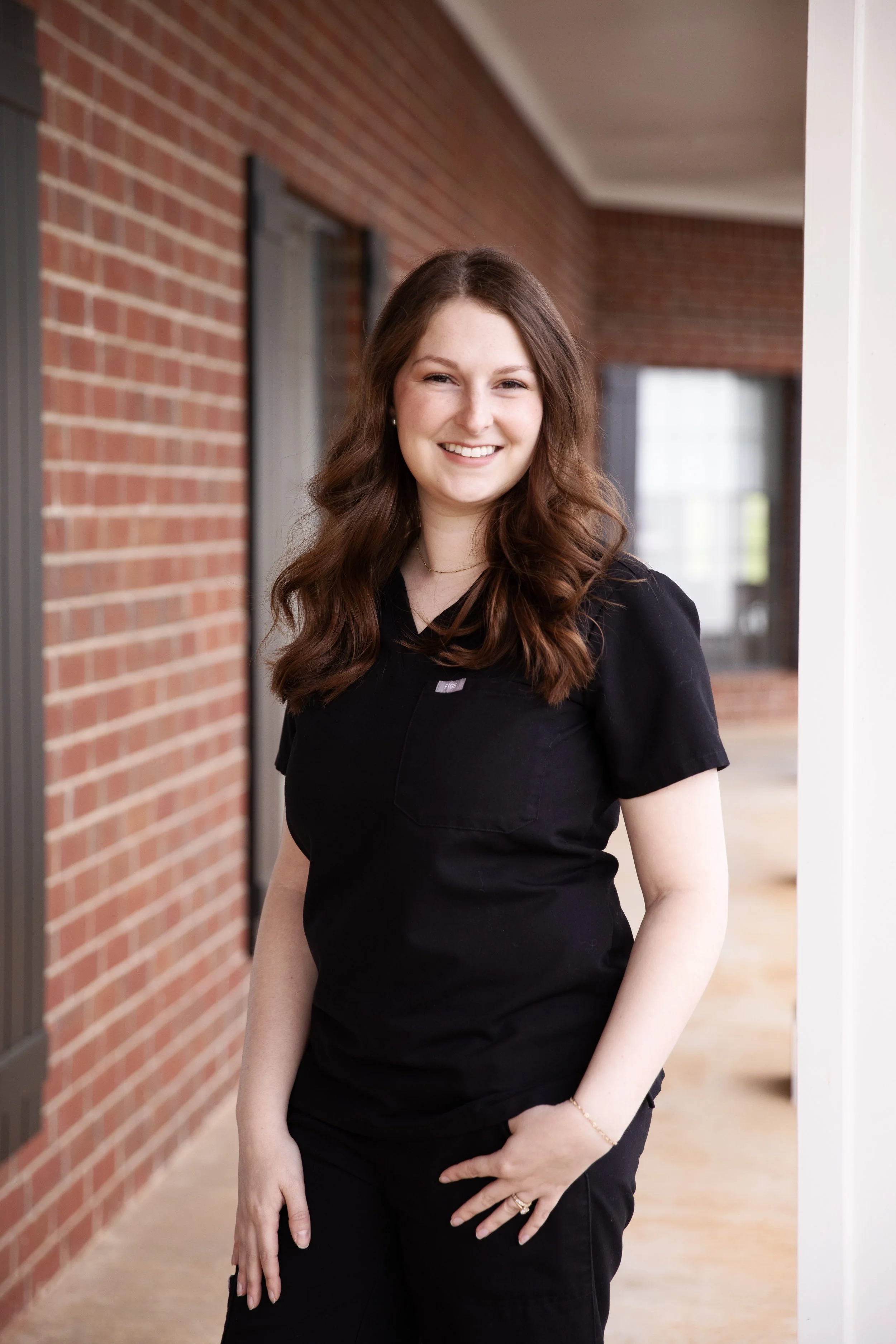 Dr. Reed, smiling at the camera, standing outside a brick building dressed in black scrubs.