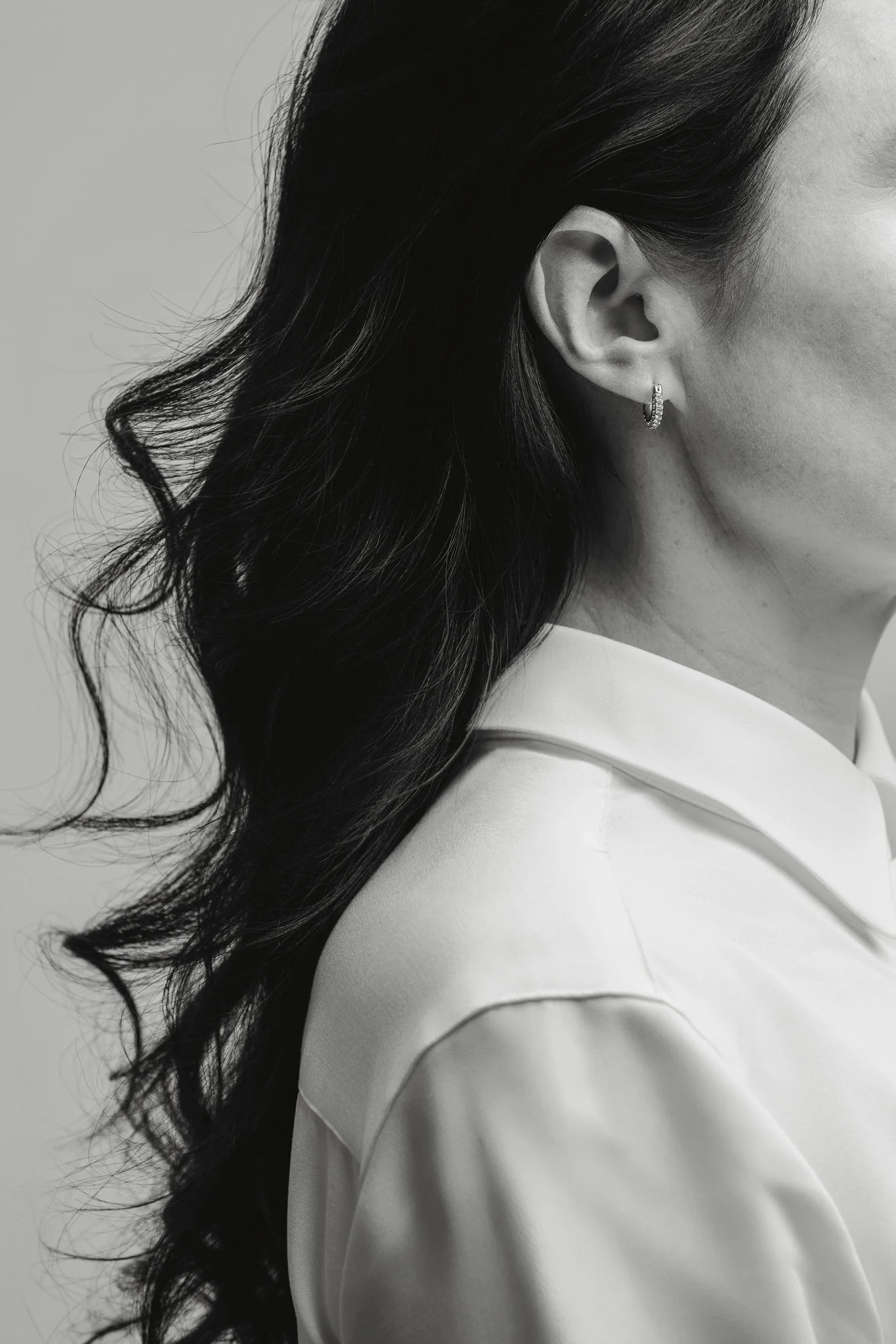 Close-up en noir et blanc d'une femme portant une boucle d'oreille, avec des cheveux longs ondulés et une robe à col.