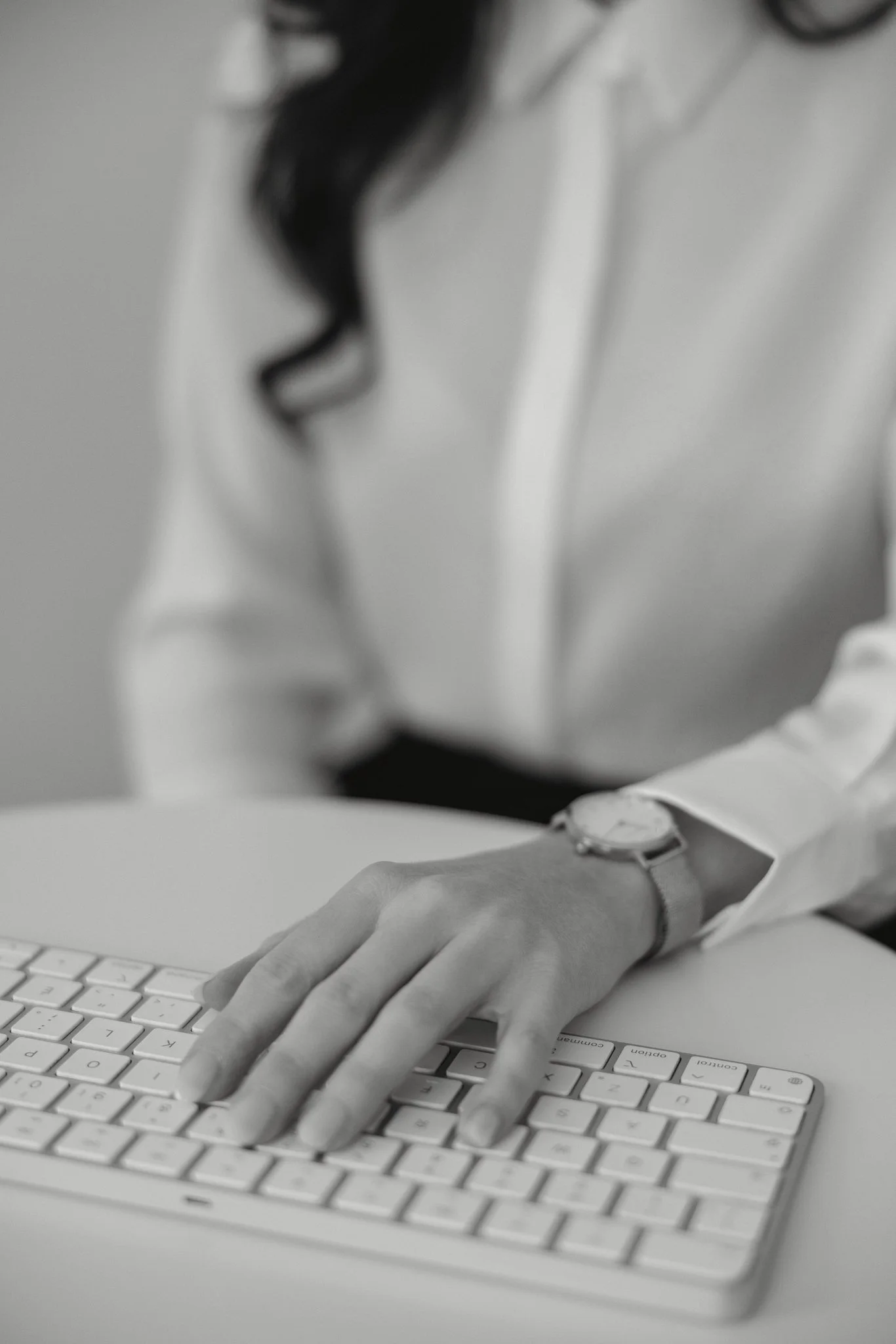 Main sur un clavier d'ordinateur, portant une montre, dans un environnement de travail.