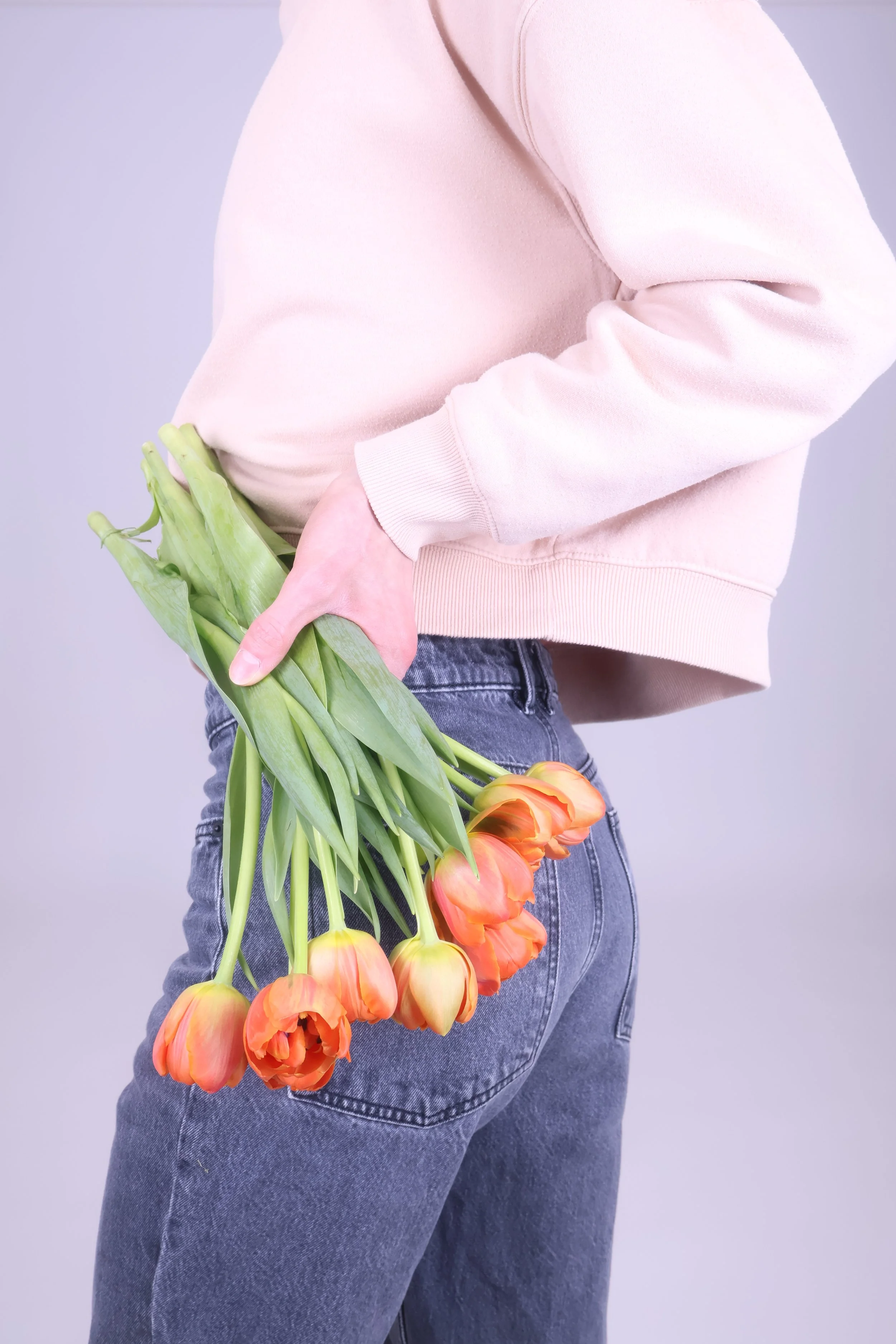 Ihminen pitää takkinsa taskussa kiinni kukkakimppua, jossa on appelsiininvärisiä tulppaaneja.