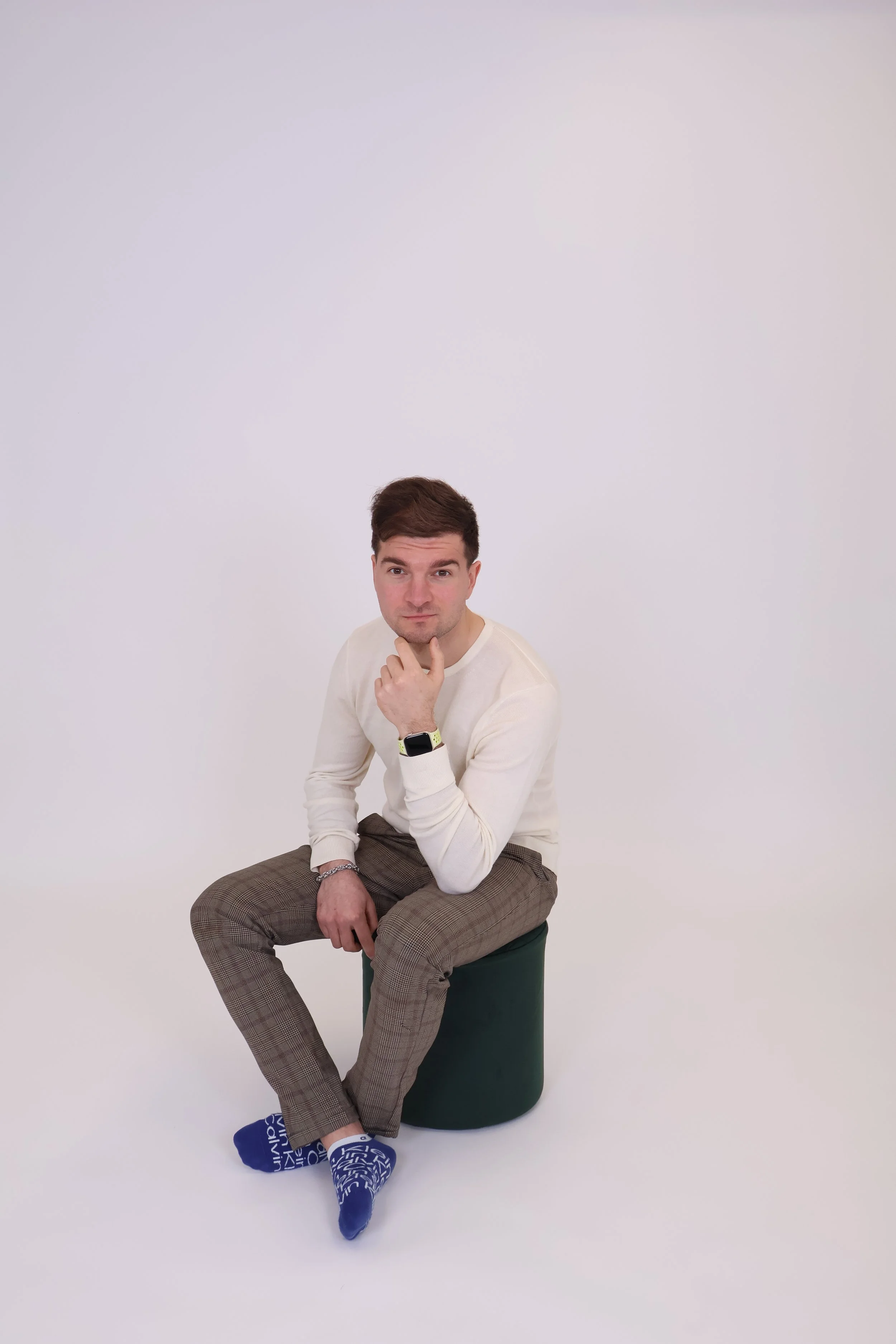 Nuori mies istuu tuolilla, pää kädessä ja katsoo kameraan, taustalla valkoinen seinä.
