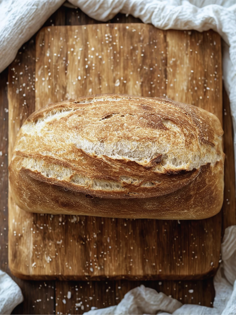 Loaf of freshly baked bread on a wooden cutting board with salt sprinkled around