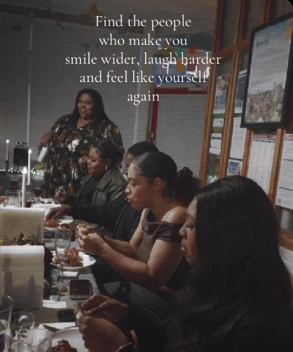 Women sitting at a dining table, eating and socialising at a supper club hosted by OK DEN CIC with framed pictures on wooden walls, and a woman standing in the background, with an inspirational quote overlay about finding happiness and connection.