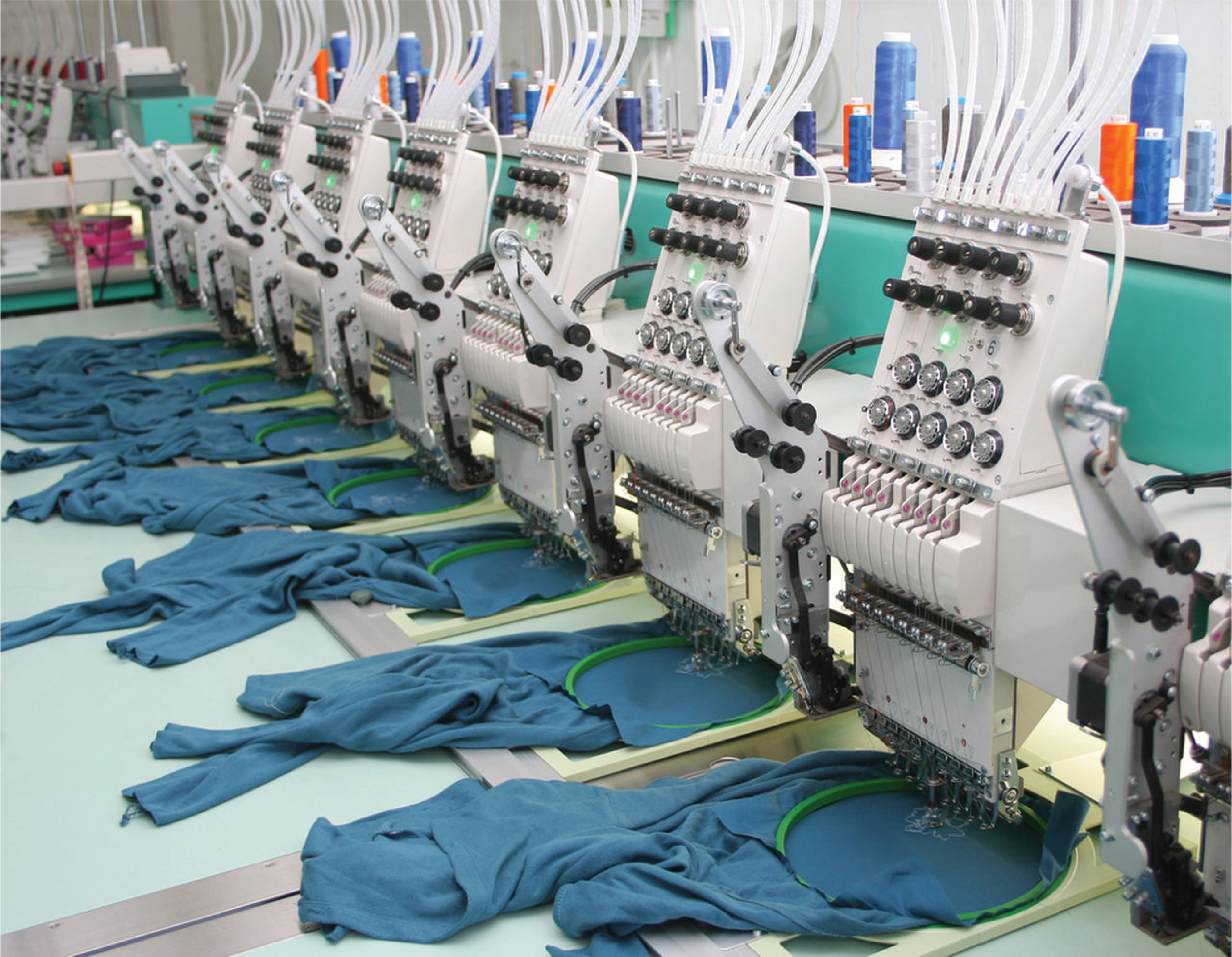 Industrial textile embroidery machines sewing blue fabric work gloves in a factory setting.