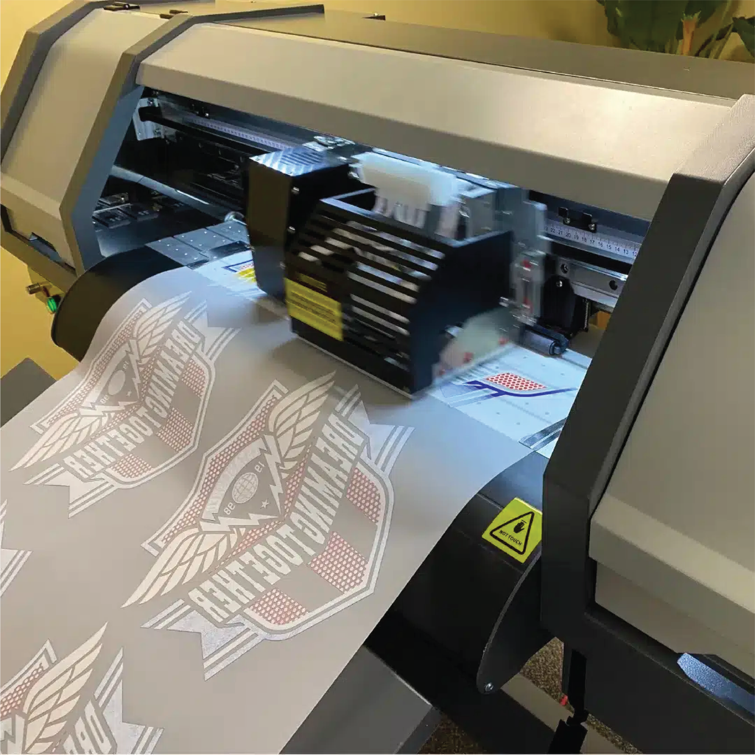 A professional-grade printer producing a printed design with Harley Davidson logos on a piece of fabric or vinyl.