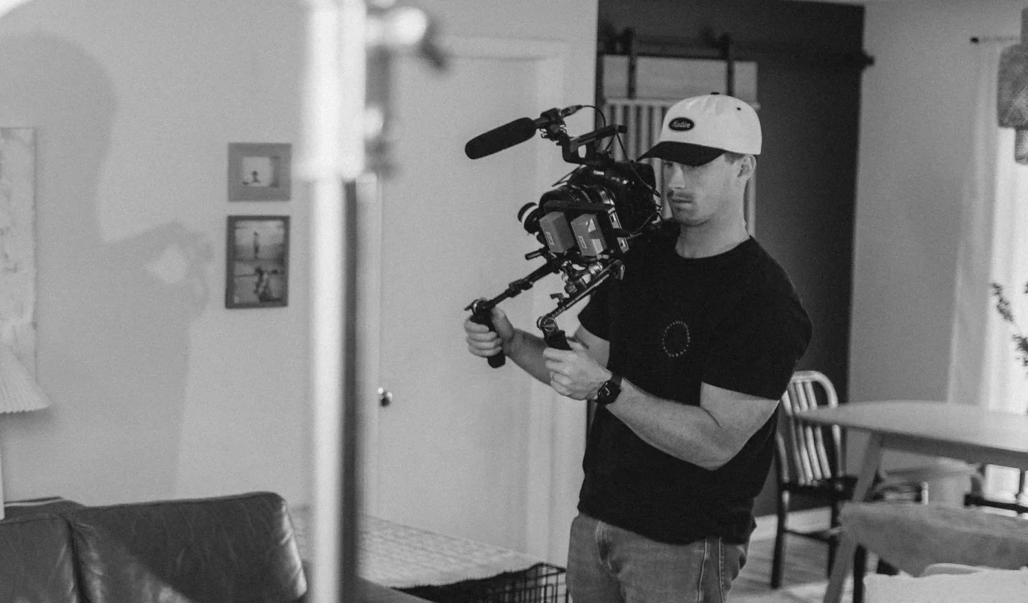 A man with a cap filming with a professional camera stabilizer inside a home.