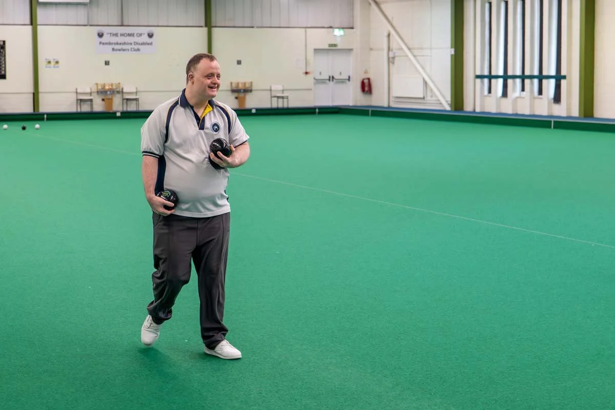 A man playing bowls on indoor green artificial turf in a bowling club.