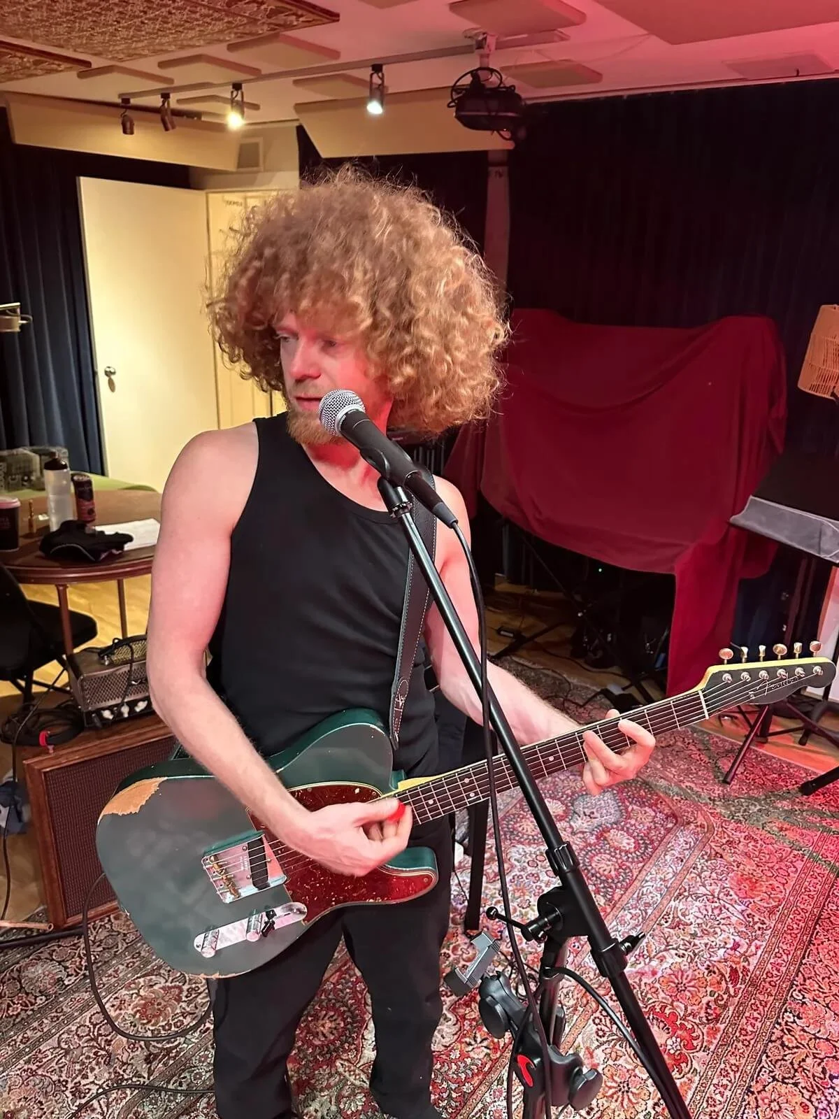 Glenn of The Needful, a man with curly hair playing an electric guitar in a music rehearsal space or studio.