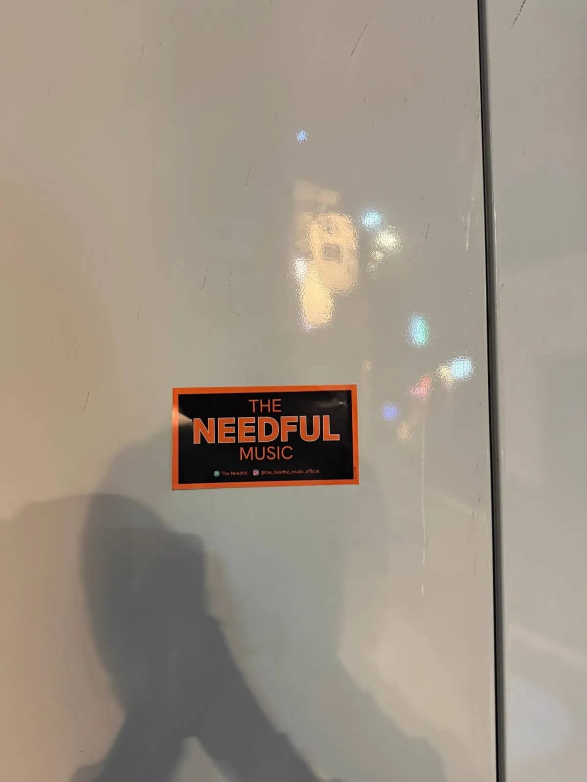 A sticker on a white surface reads 'The Needful Music' in orange and black colors.