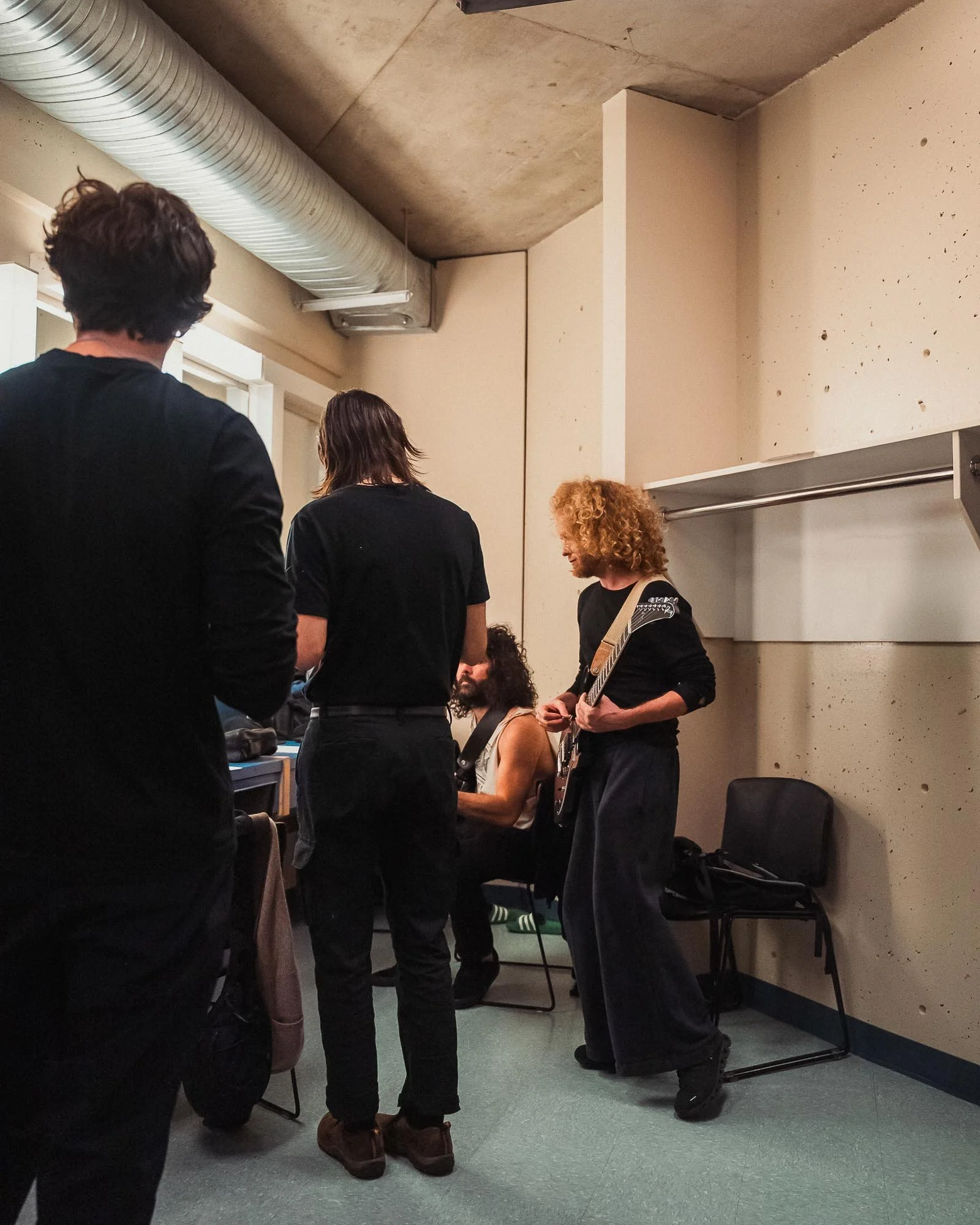 A Canadian musical group called The Needful standing closely together in a backstage room, some holding musical instruments.