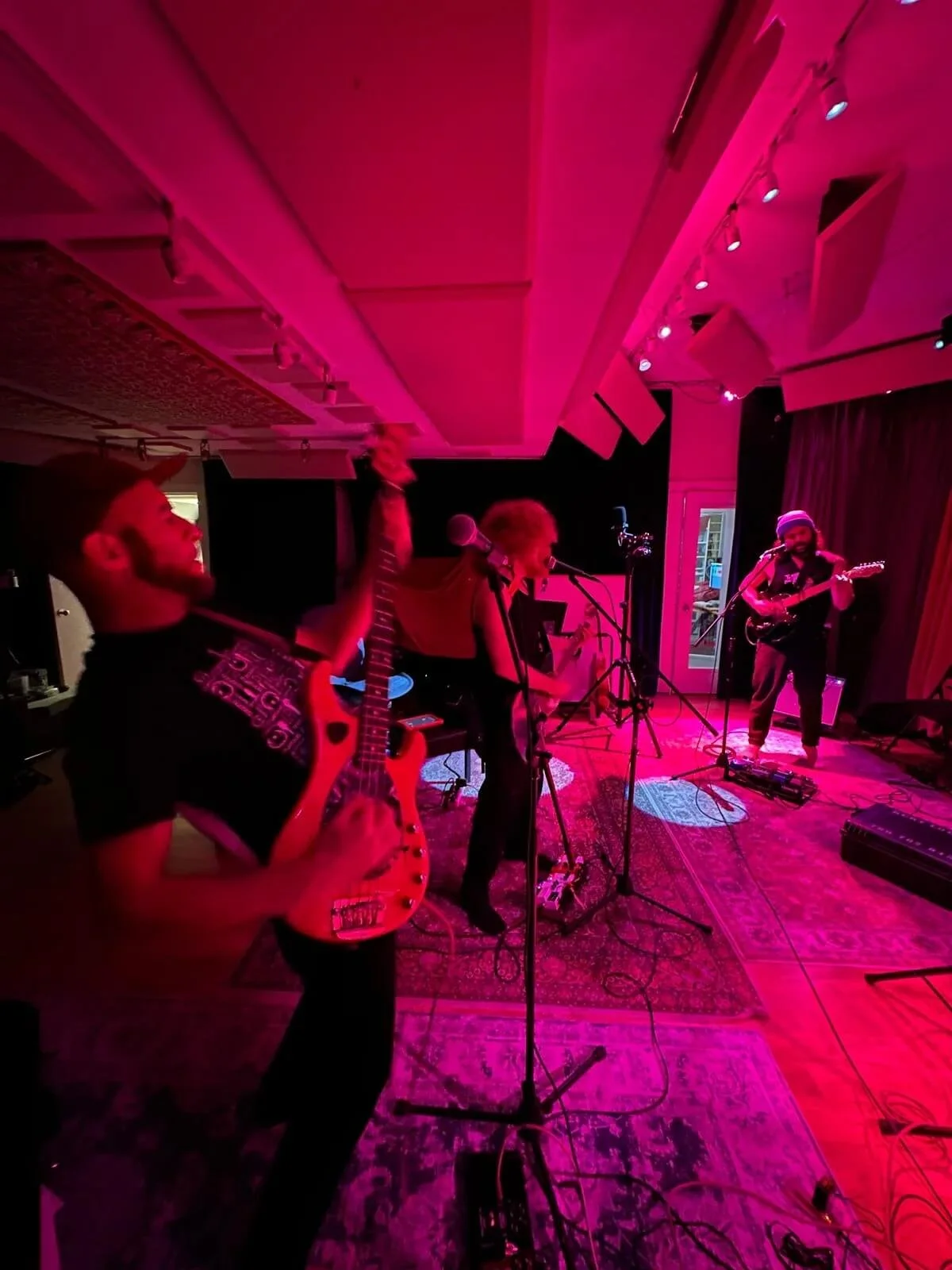 The Needful band performing on stage with pink lighting, playing guitars and singing.