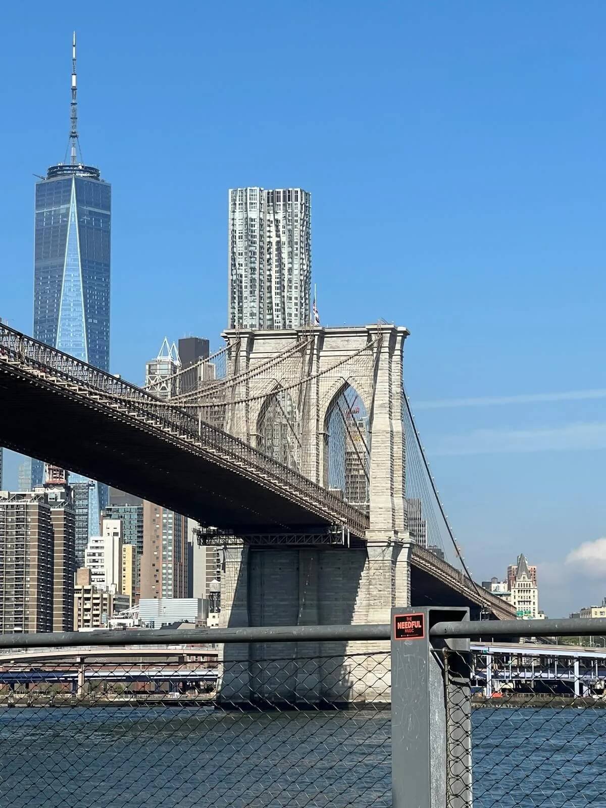 View of the Brooklyn Bridge with New York City skyscrapers, including One World Trade Center, in the background on a clear day.