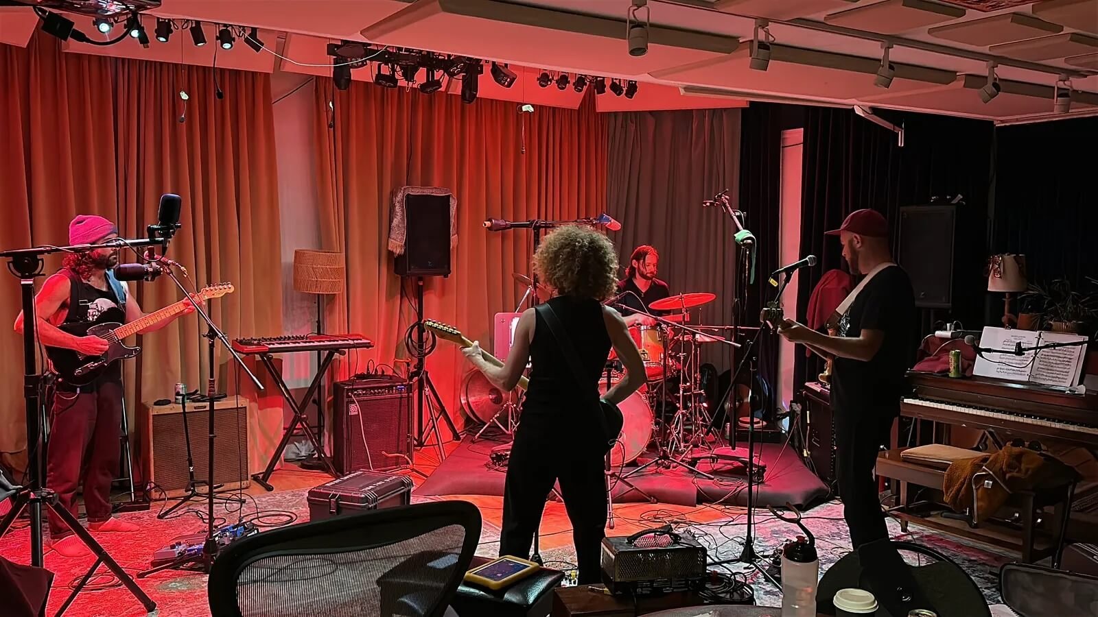 The Neeful band practicing on stage, facing eachother with orange lighting