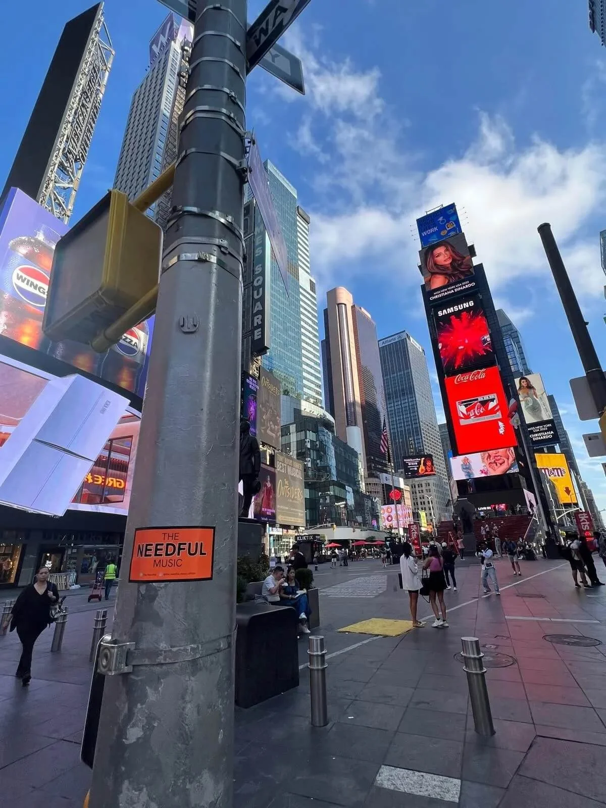 View of Times Square in New York City featuring tall buildings, digital billboards, and people walking on the street on a sunny day.