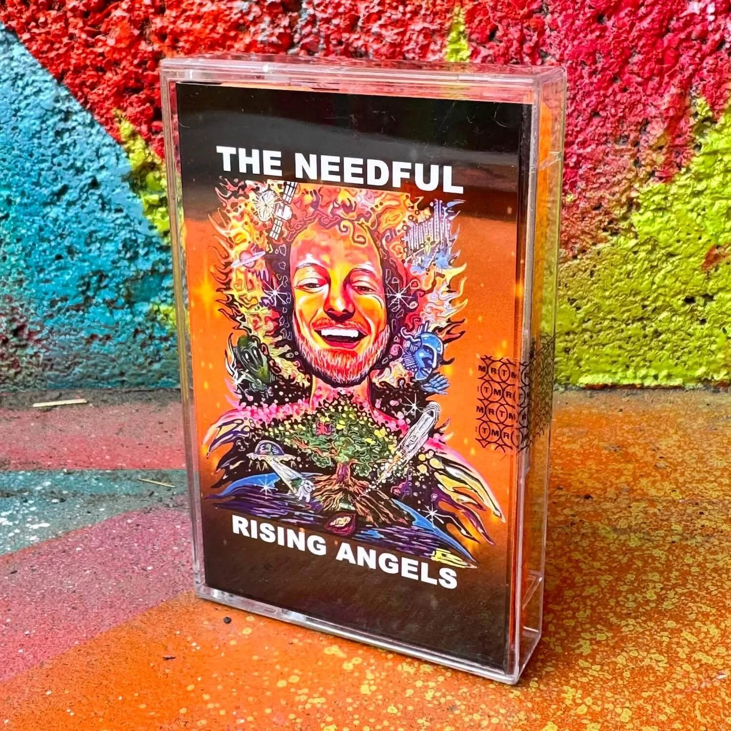 A colorful poster featuring a smiling cartoon face with flames in the hair, surrounded by various objects and symbols related to technology, space, and science. The poster includes the text "THE NEEDFUL RISING ANGELS".