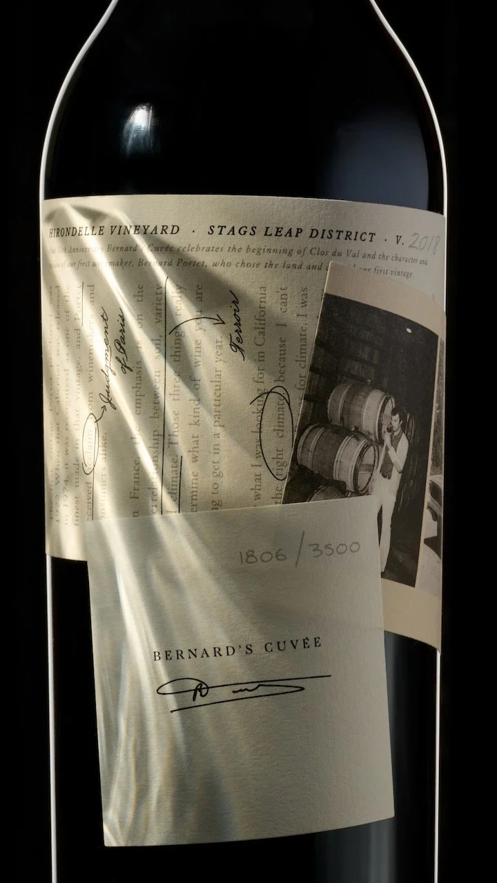 A wine bottle with a label from Bernard's Cuvée, featuring a handwritten edition number 1806/3500, and a photograph of wine barrels attached to the label.
