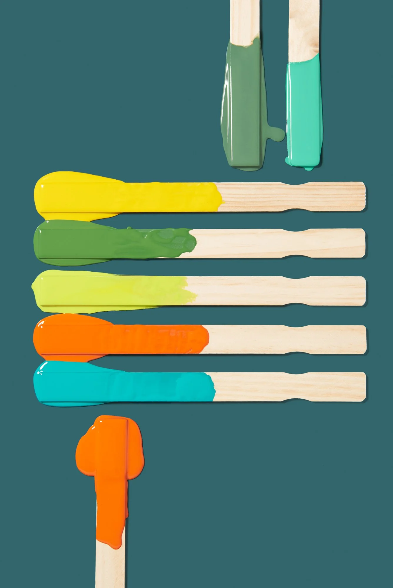 Colorful paint stirrer sticks painted with different colors in a vertical arrangement on a teal background, with three additional sticks at the top and one large orange painted stick at the bottom.