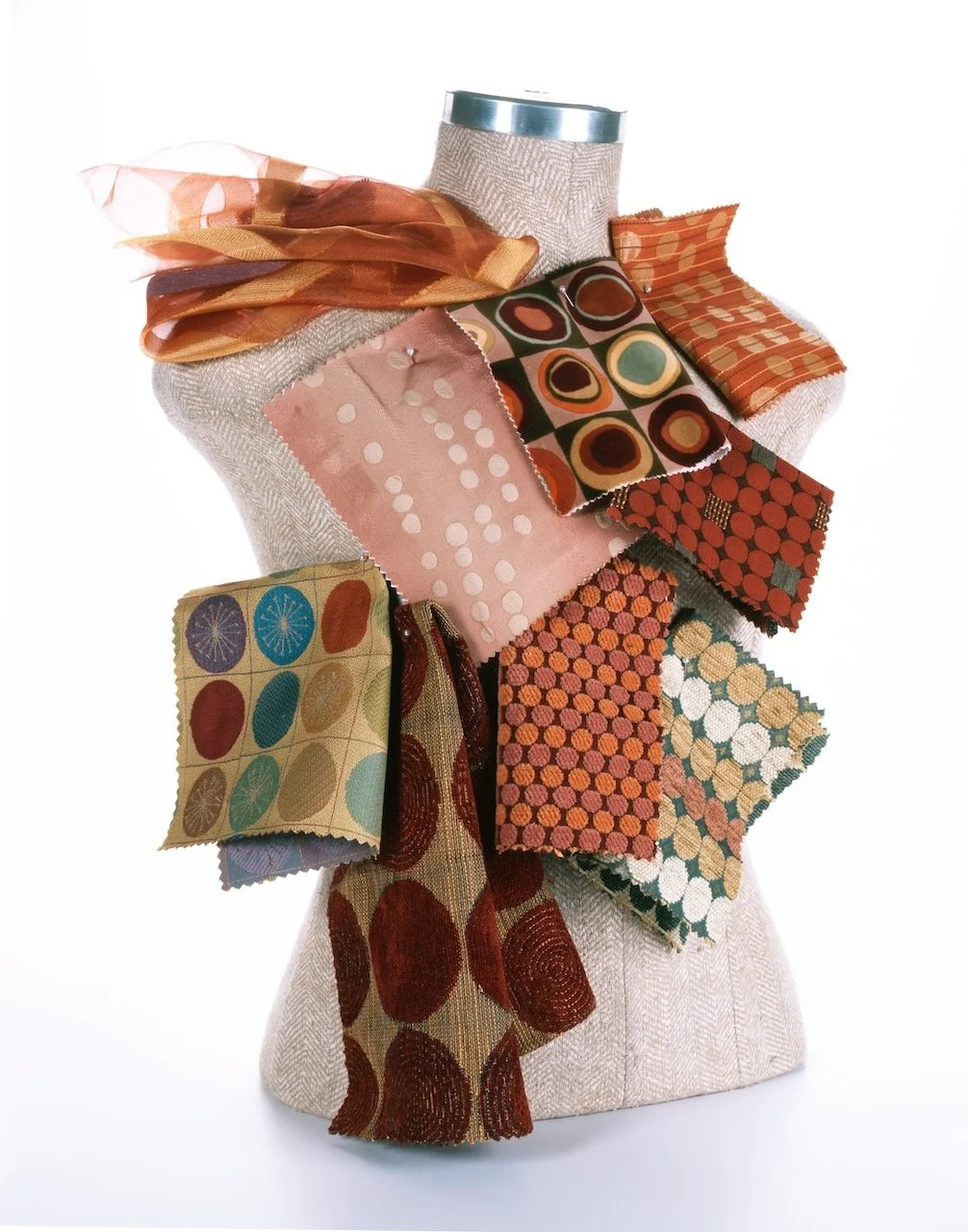 A fabric-covered mannequin bust decorated with various colorful fabric swatches, scarves, and trims in warm earth tones, including reds, oranges, browns, and greens.