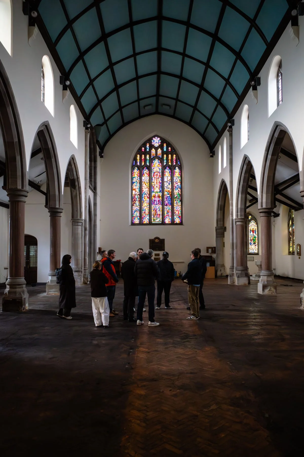Group of people inside a church with stained glass windows and high vaulted ceiling.