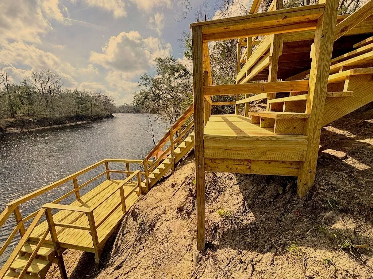 Wooden staircase and deck overlooking a river with trees and a partly cloudy sky.