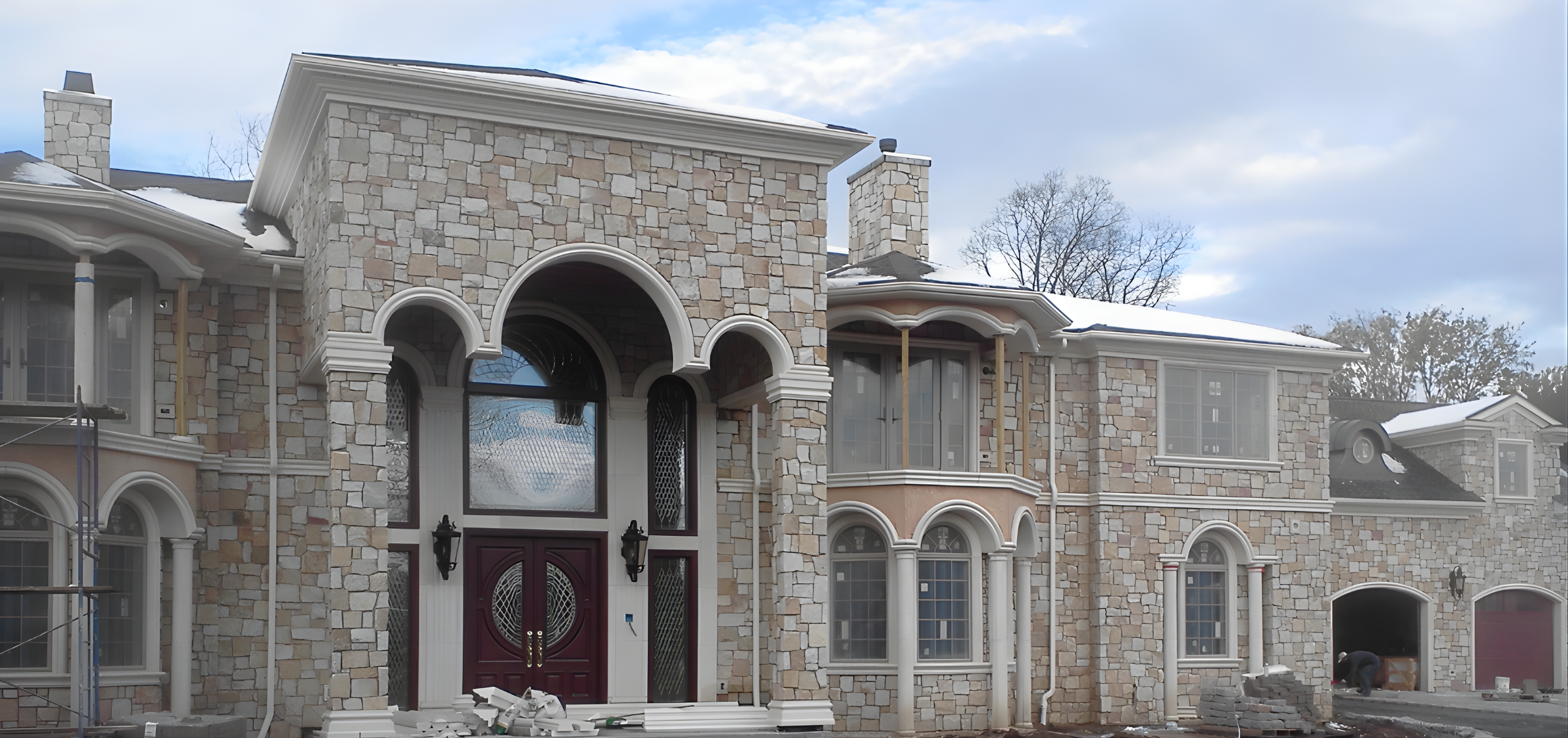 A large house under construction with stone exterior, arched windows, and a front door. 