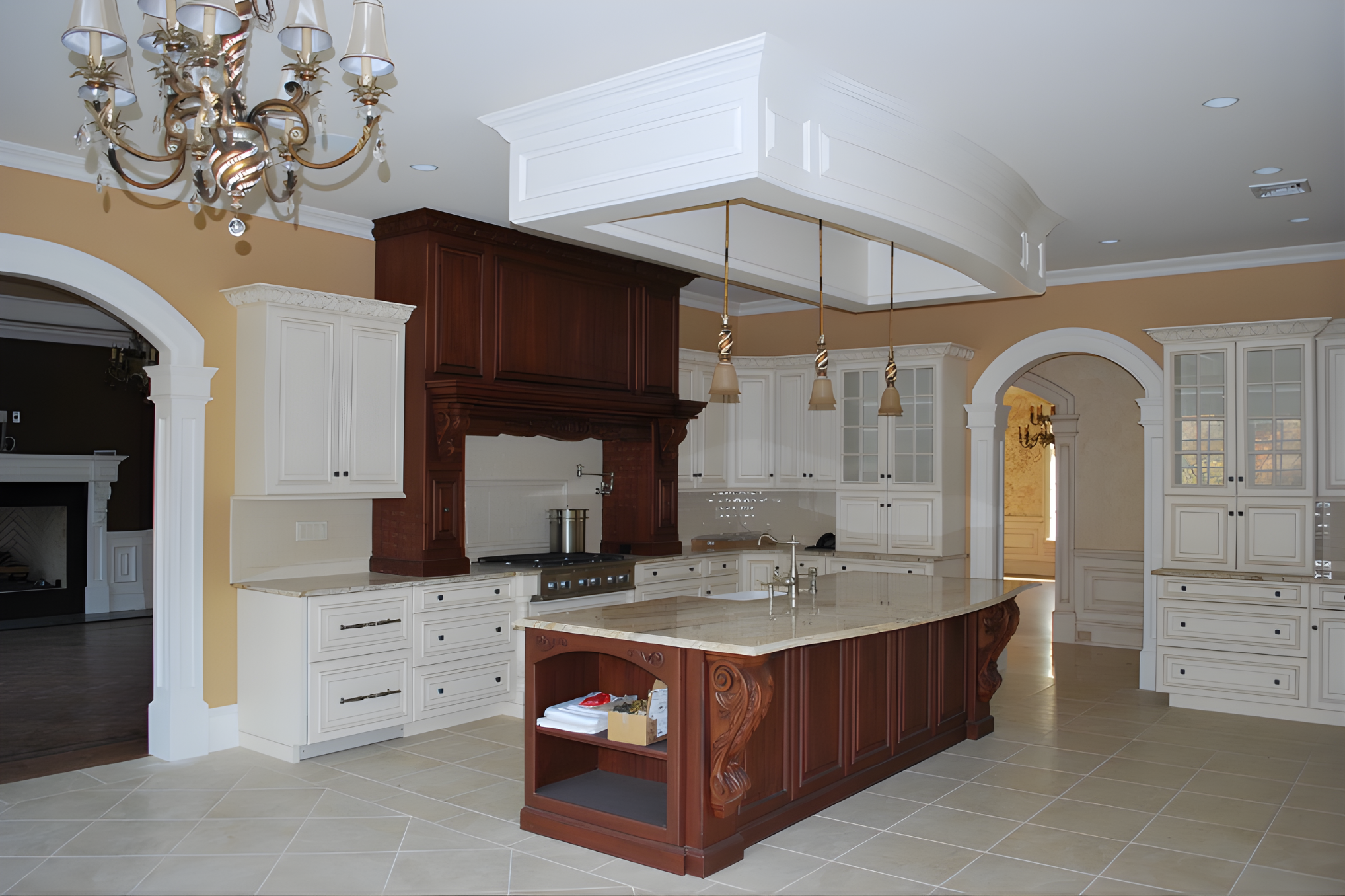 A spacious kitchen with a central island featuring a marble countertop and wooden base, surrounded by white cabinetry and a ceiling-mounted chandelier.