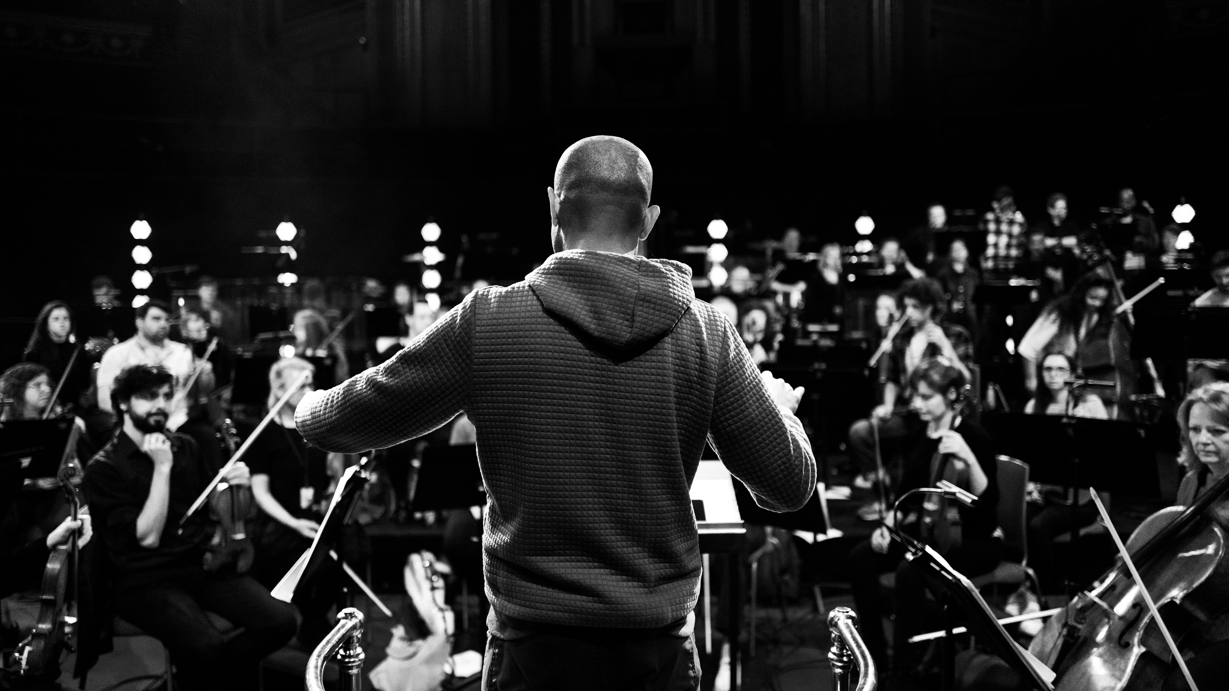 Orchestra conductor leading a large orchestra during rehearsal or performance in a concert hall.