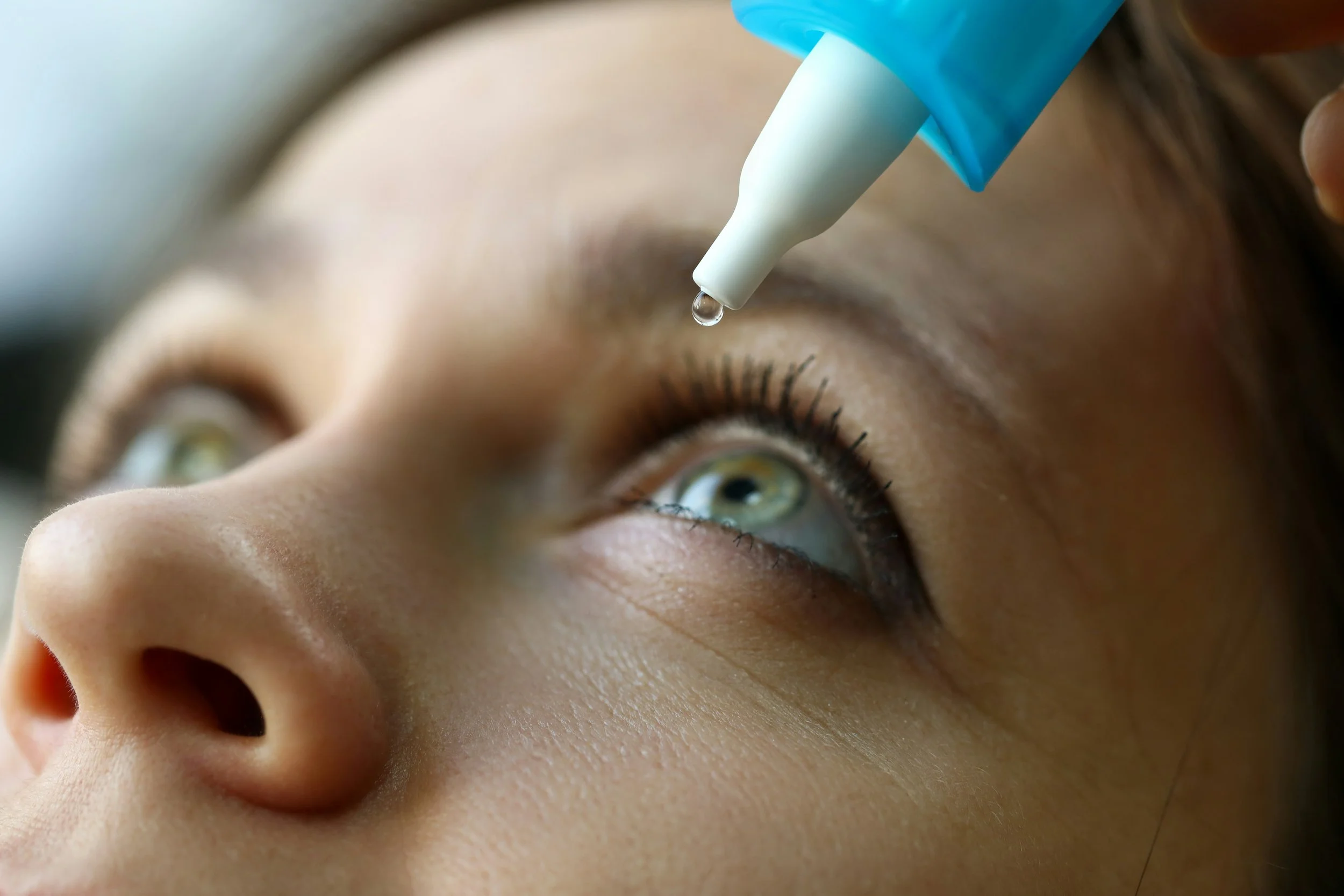 Close-up of a person receiving an eye drop, showing their eye and nose.