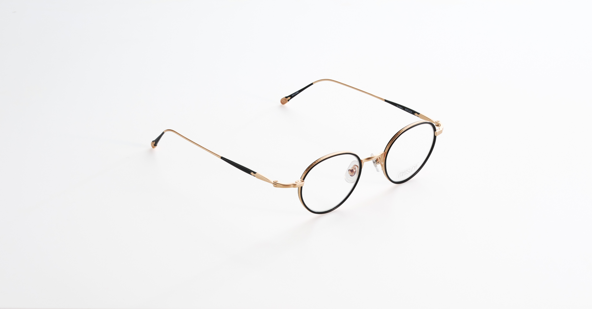 A pair of Matsuda round eyeglasses with a gold and black frame on a white background.